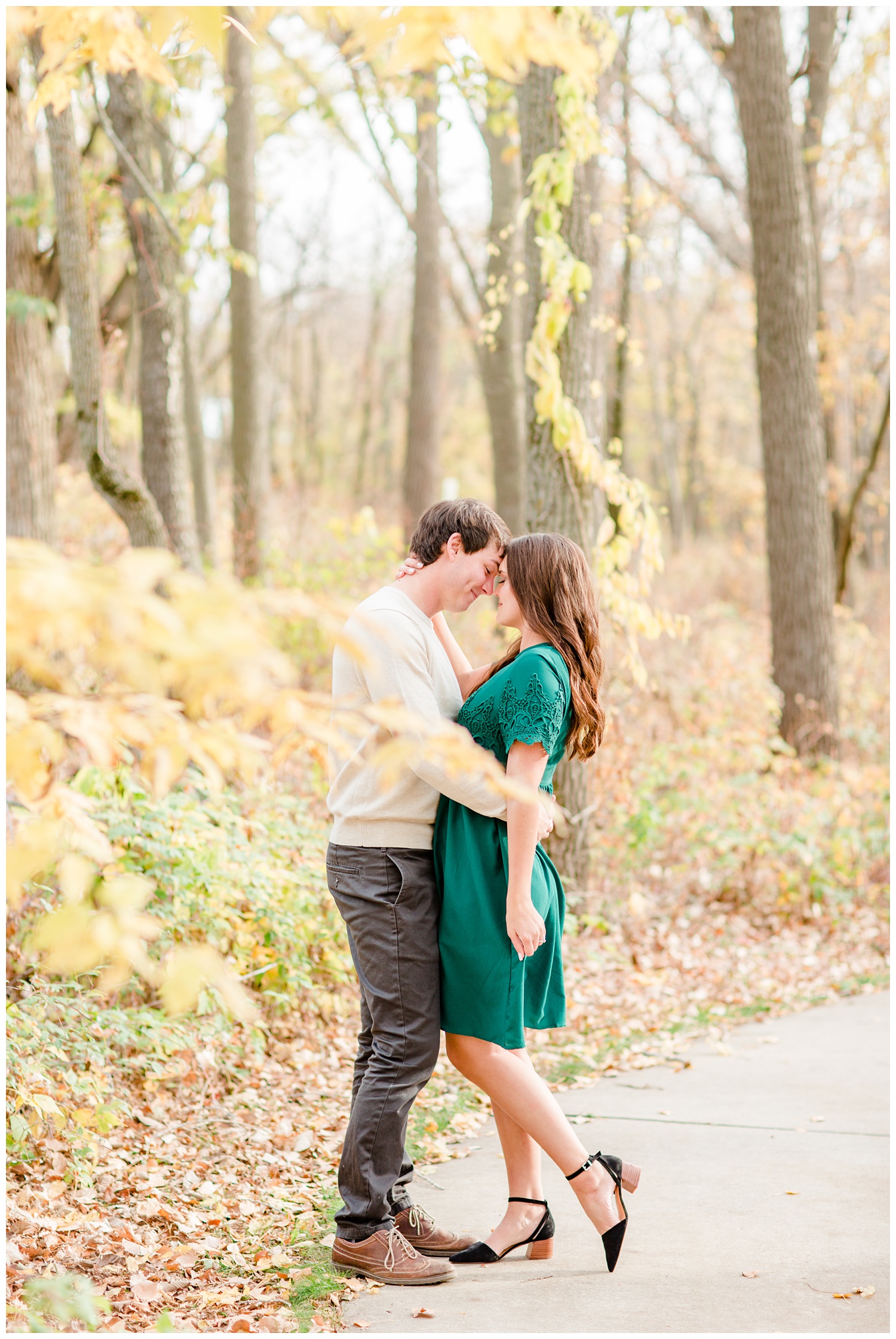 Fall in Iowa, Jenna wearing an emerald green dress embraces Brady in the middle of an autumn path at Lost Island Nature Center | CB Studio