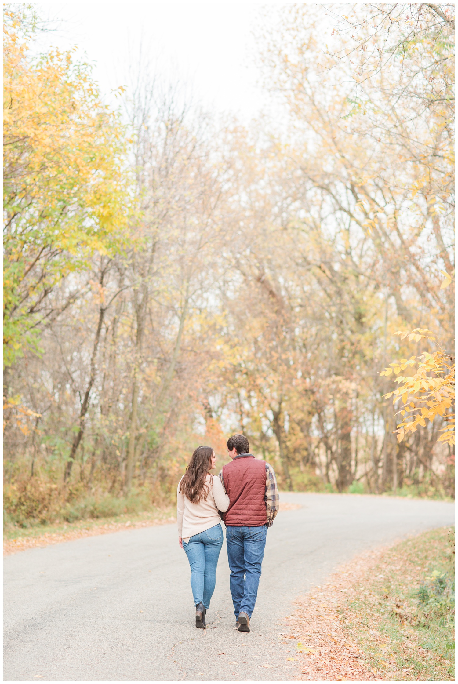 Fall in Iowa, Jenna and Brady link arms as they walk along an autumn path at Lost Island Nature Center | CB Studio