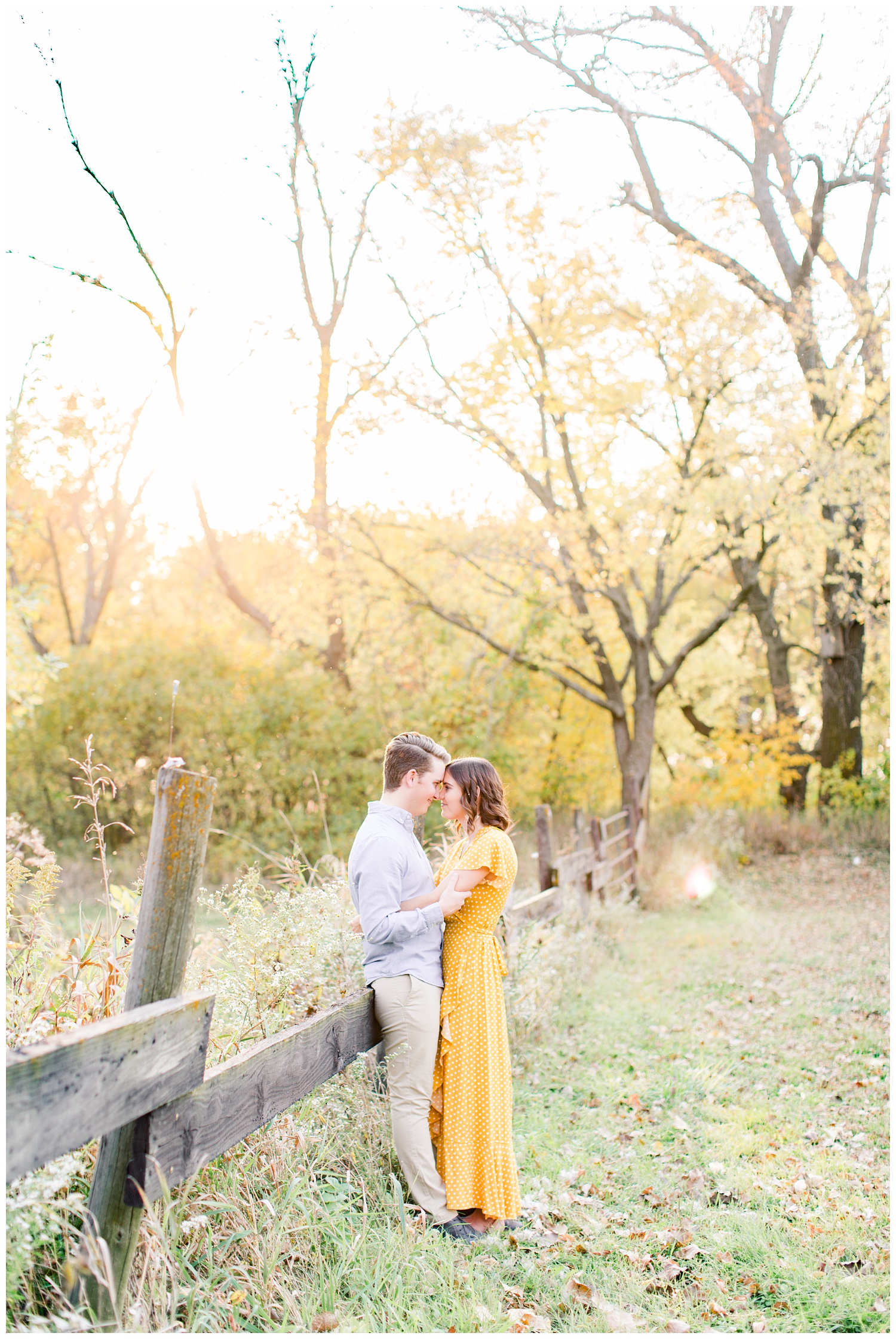 Jadi and Luke lean against a wooden fence post in a grassy field in Iowa during the fall for engagement photos | CB Studio