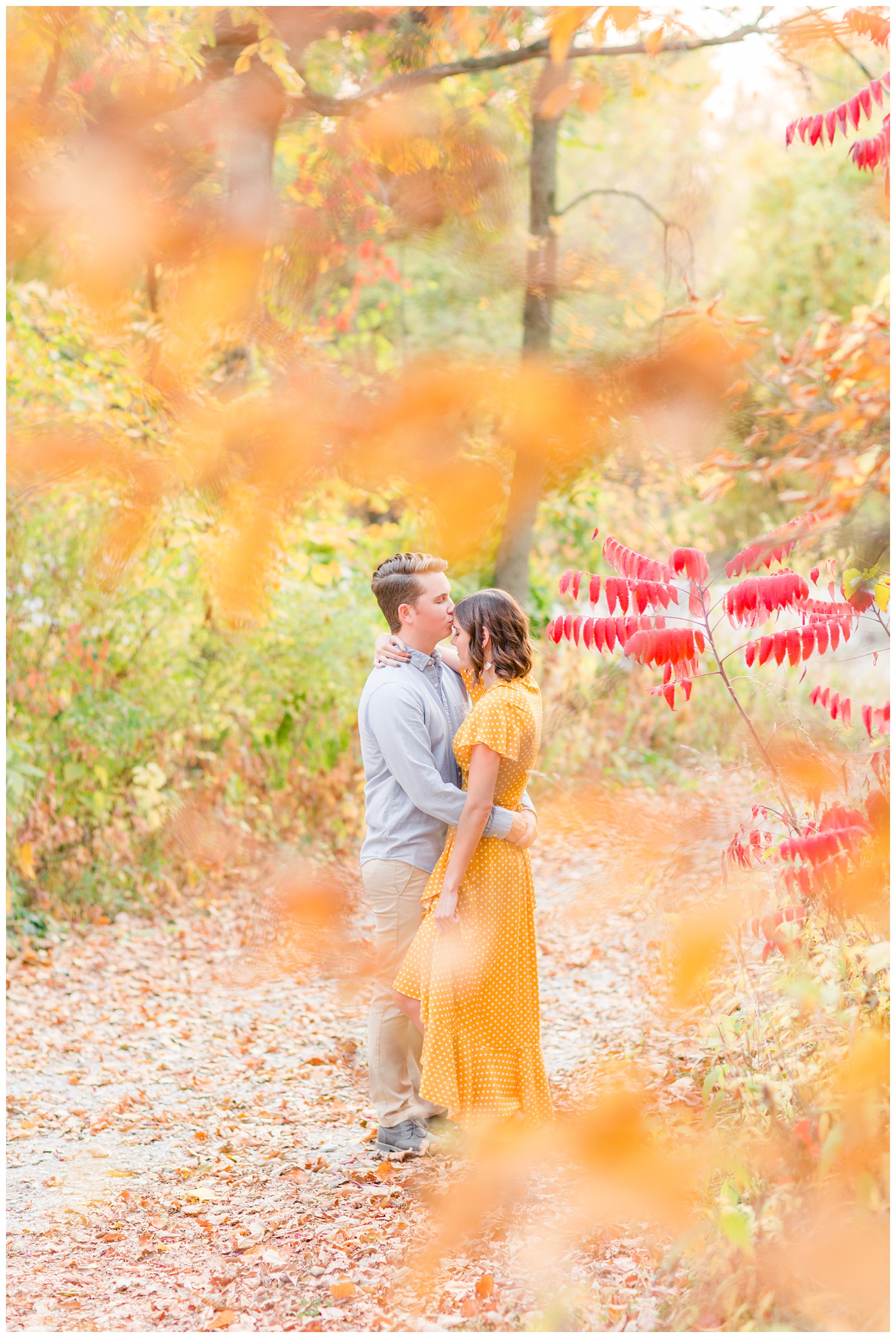 Jadi wearing a yellow flowing dress looks down as Luke kisses her forehead while embracing together in a grassy field in Iowa during the fall for engagement photos | CB Studio
