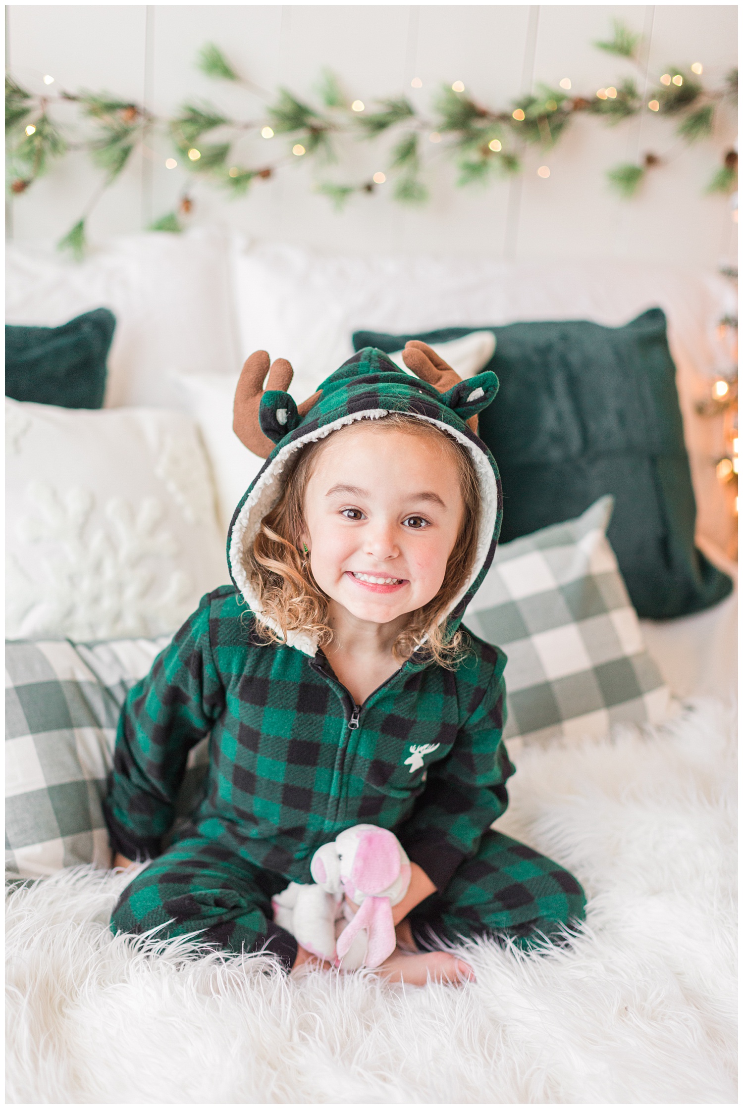 Sadie, wearing an emerald green plaid moose sleeper pajamas, sits on a green Christmas themed bed | CB Studio