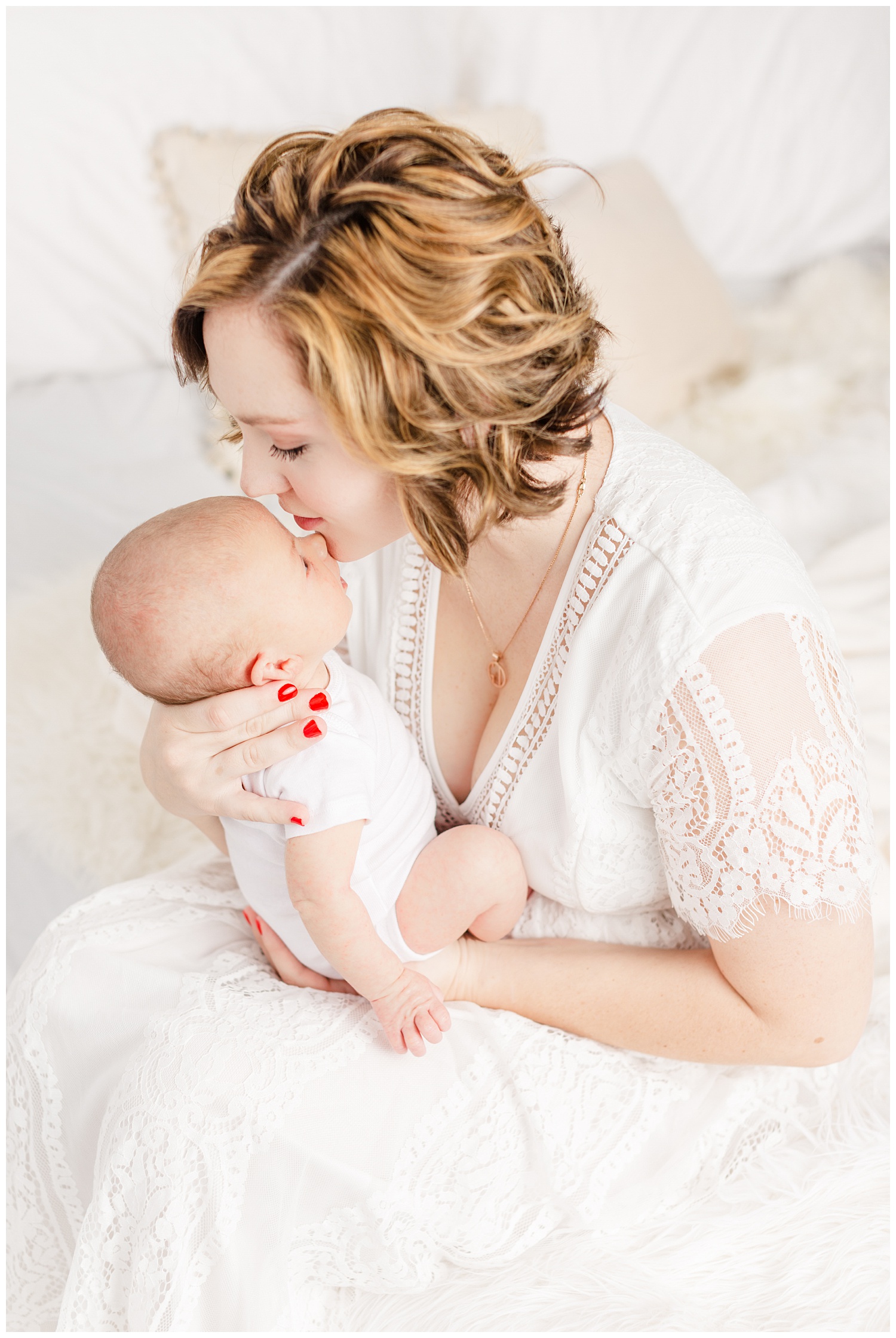 Bree dressed in white lace sits on her bed and gently kisses her new baby boy | CB Studio