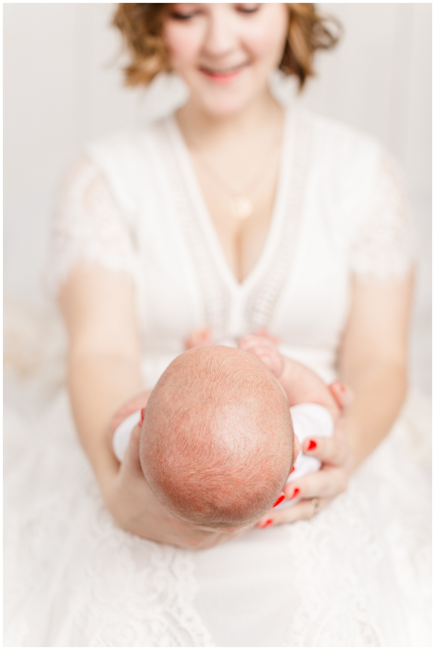 Bree dressed in white lace sits on her bed and smiles at her new baby boy | CB Studio