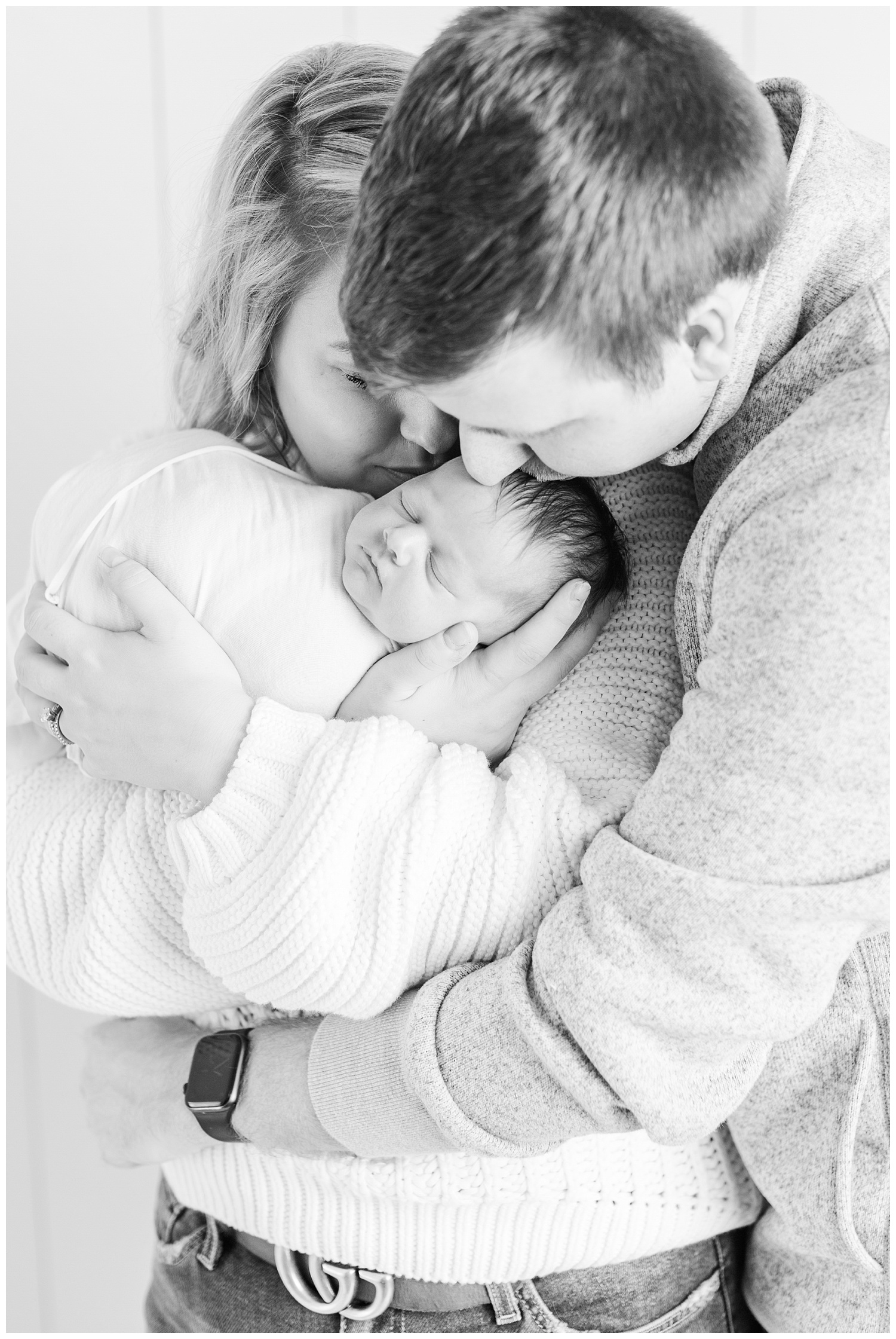 Mom and dad snuggle their newborn baby girl and gently kiss her head. | CB Studio