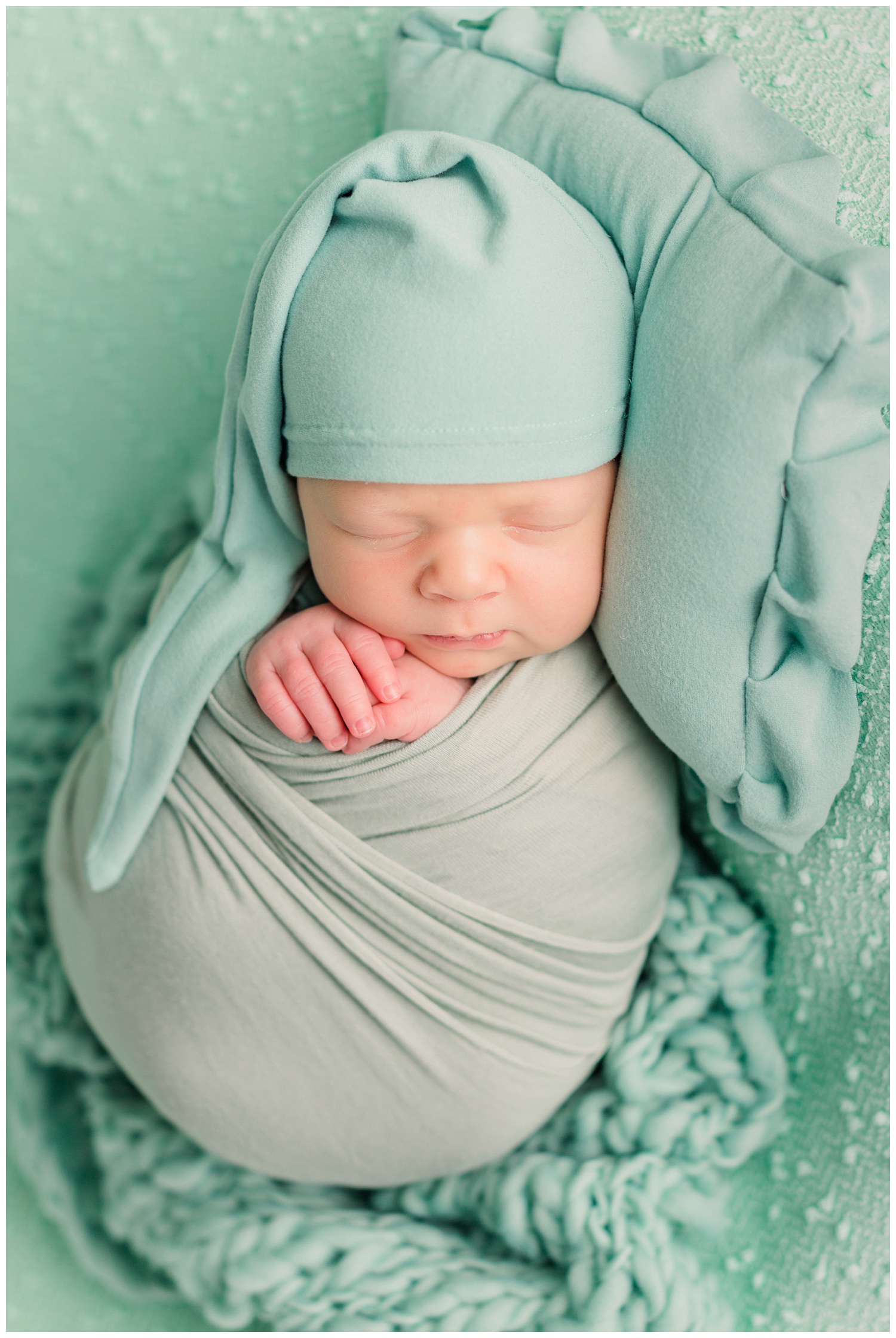 Baby boy Theo wrapped in mint green wearing a mint green night cap nestled on a mint green background fabric and pillow | CB Studio