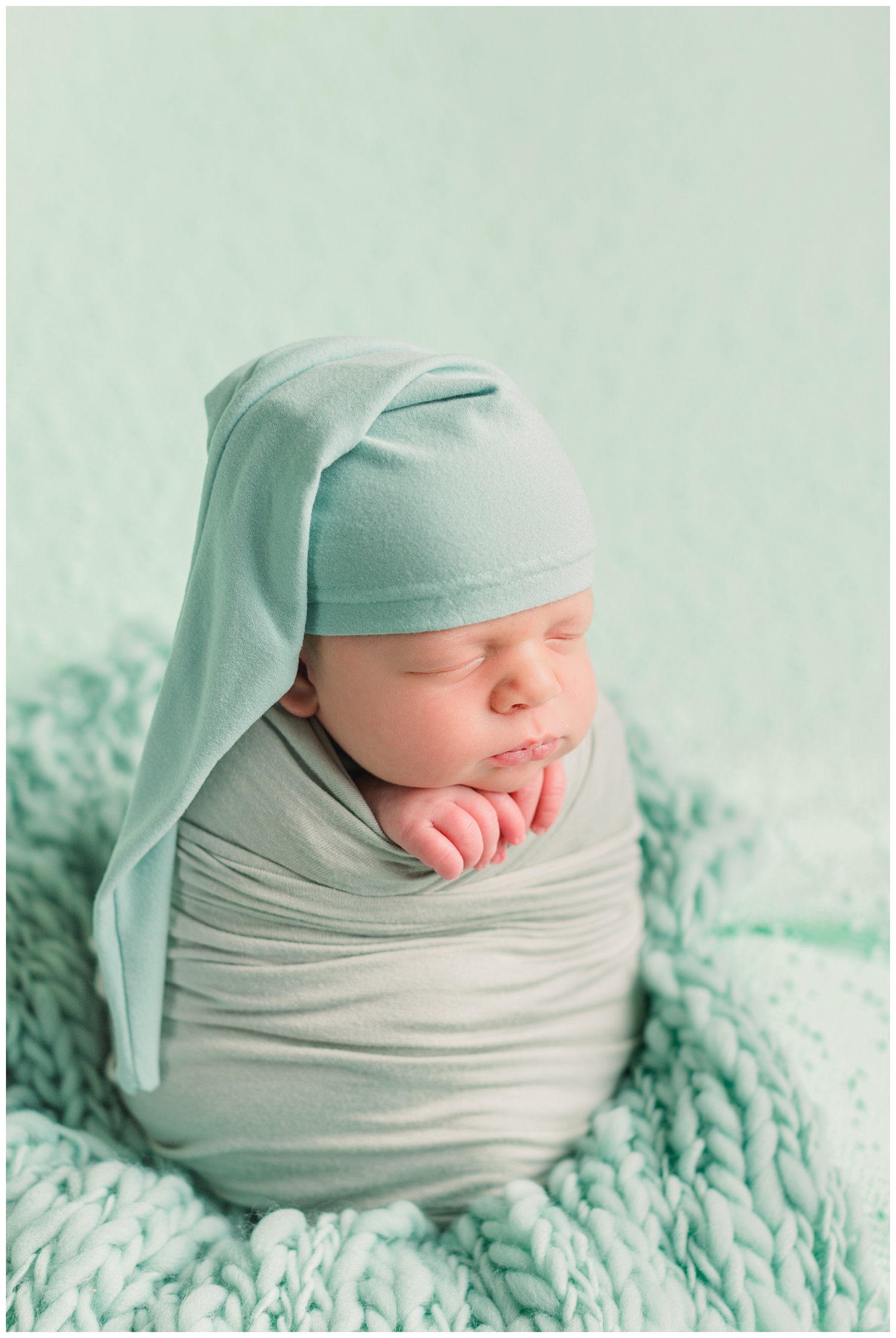 Baby boy Theo wrapped in mint green wearing a mint green night cap nestled in a potato sack pose on a mint green background fabric | CB Studio