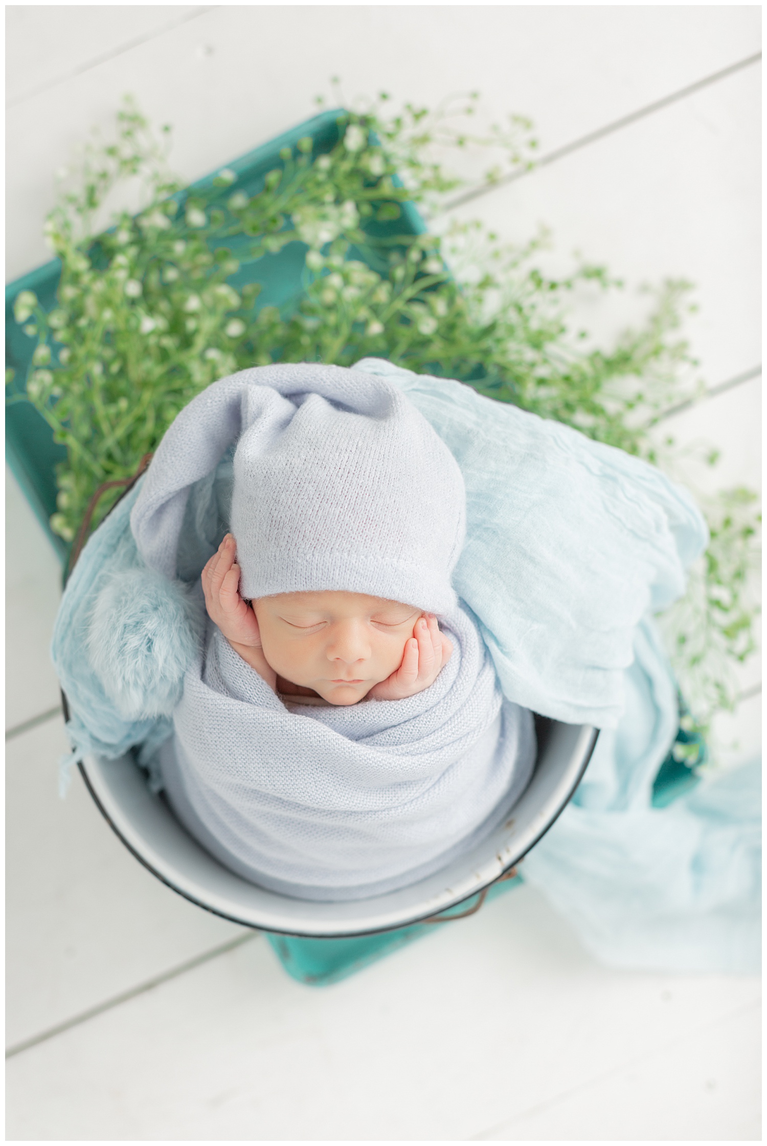 Baby boy Hayes lays in a bucket surrounded with greenery while swaddled in a soft knit blue wrap and night cap | CB Studio