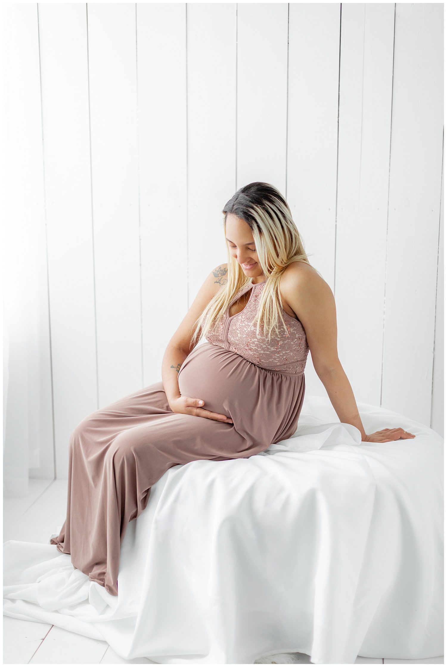 Karen patiently waits for the arrival of her baby girl while lounging on a white ottoman and wearing a blush maxi dress | CB Studio