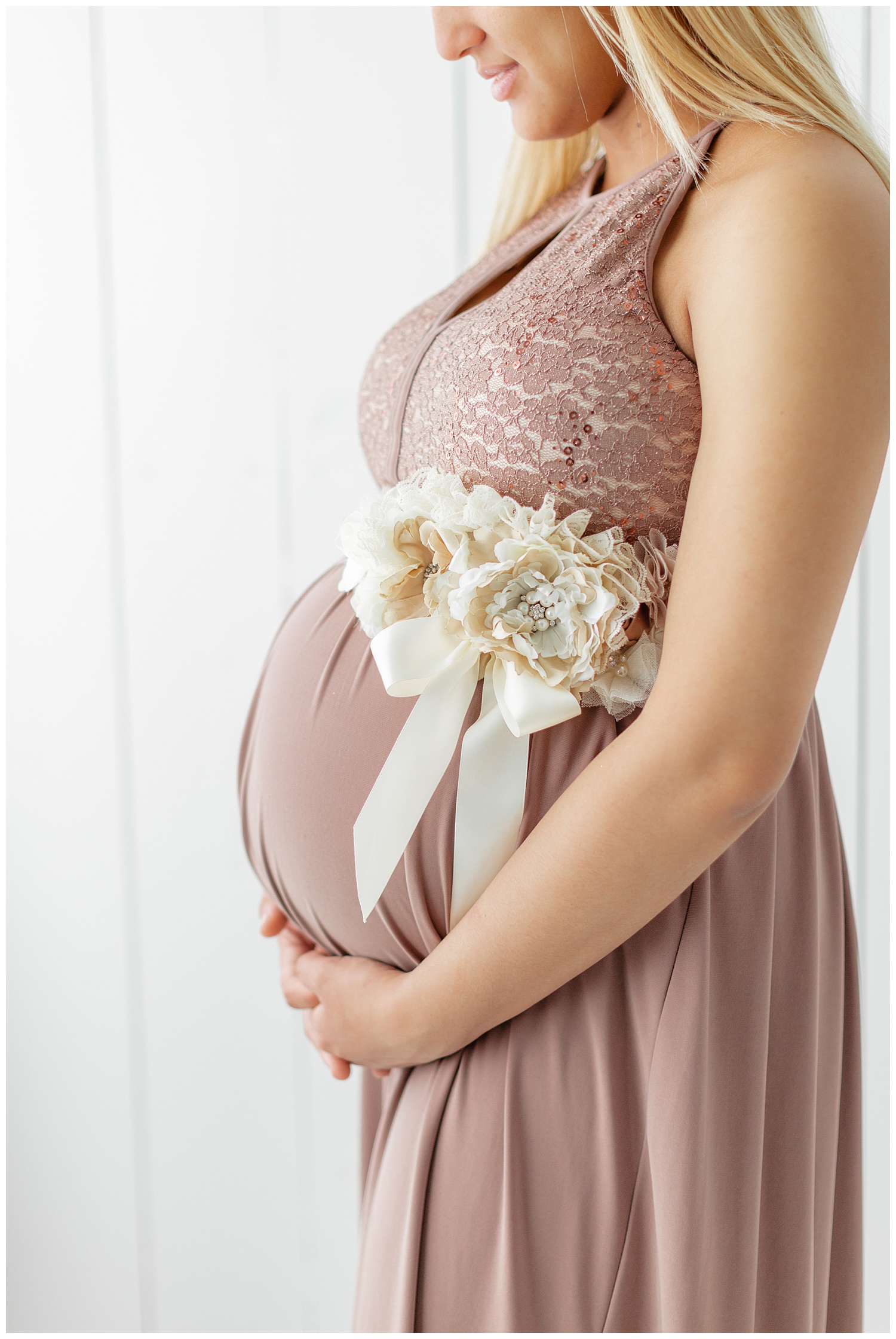 Karen patiently waits for the arrival of her baby girl while while hugging her belly adorn with a cream floral sash wearing a blush maxi dress | CB Studio
