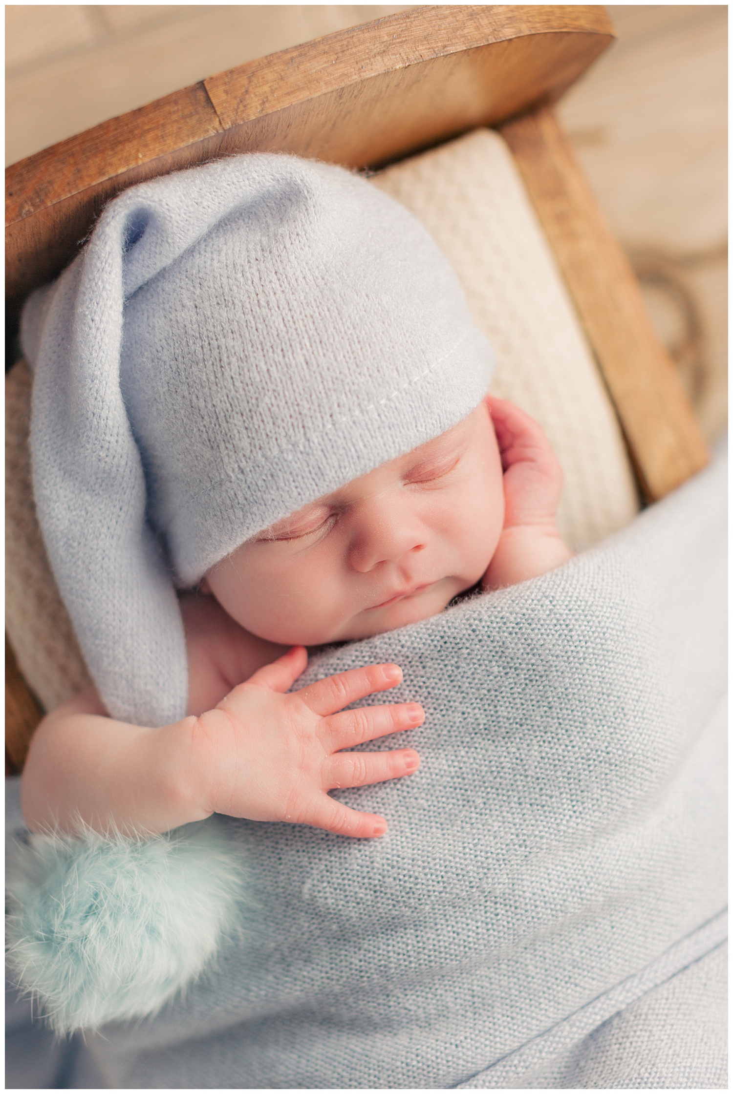 Baby Mason nestled in a wooden cradle wearing a soft blue night cap and swaddle | CB Studio