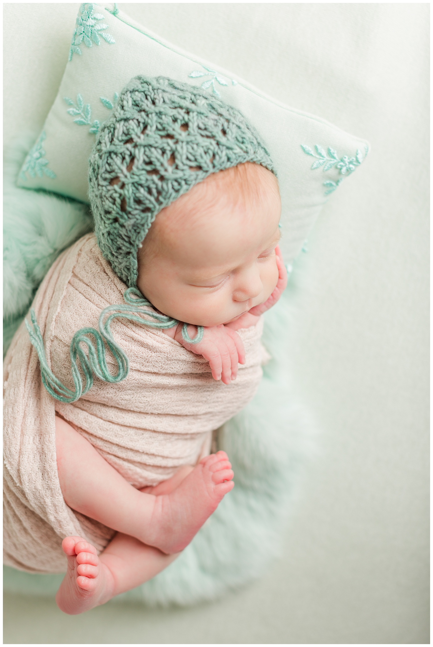 Baby Scarlett wrapped in a nude waffle knit wrap wearing a mint crocheted bonnet nestled on a mint backdrop with mint fur and pillow | CB Studio