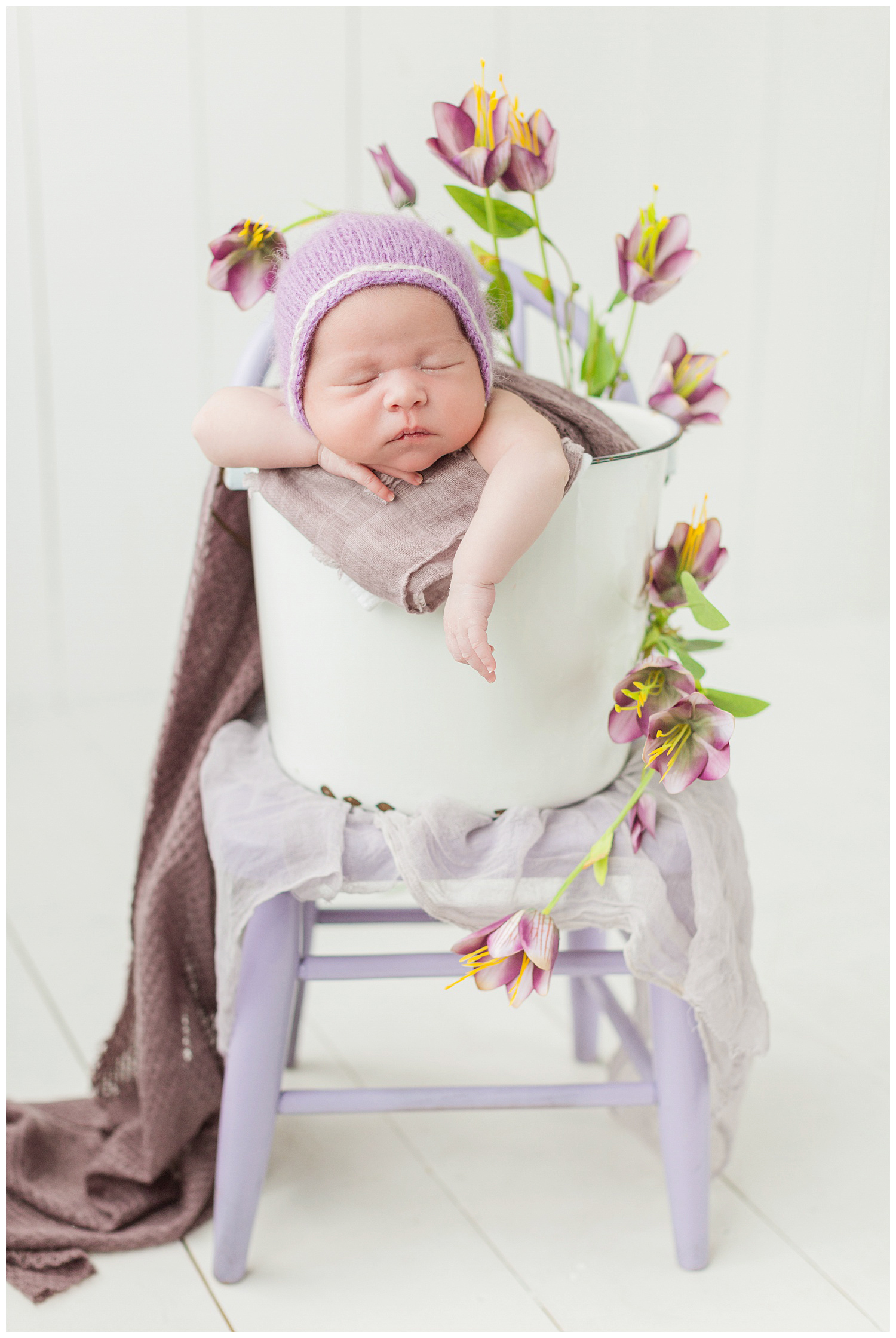 Baby Emma nestled in a bucket pose with purple florals surrounding her | CB Studio
