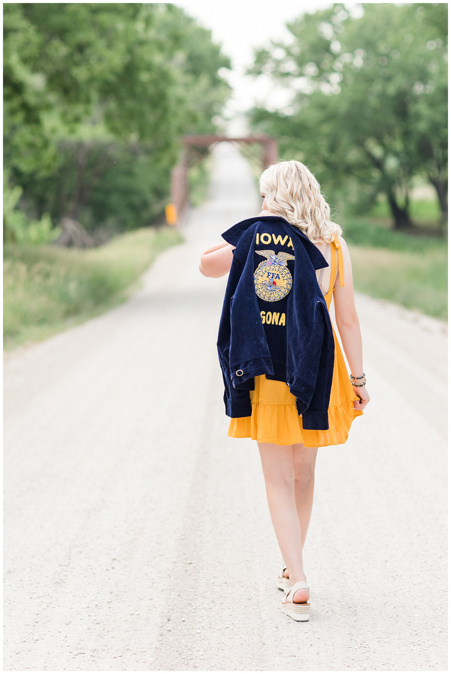Senior girl Molly walks away on a gravel road with her FFA jacket over her shoulder | CB Studio