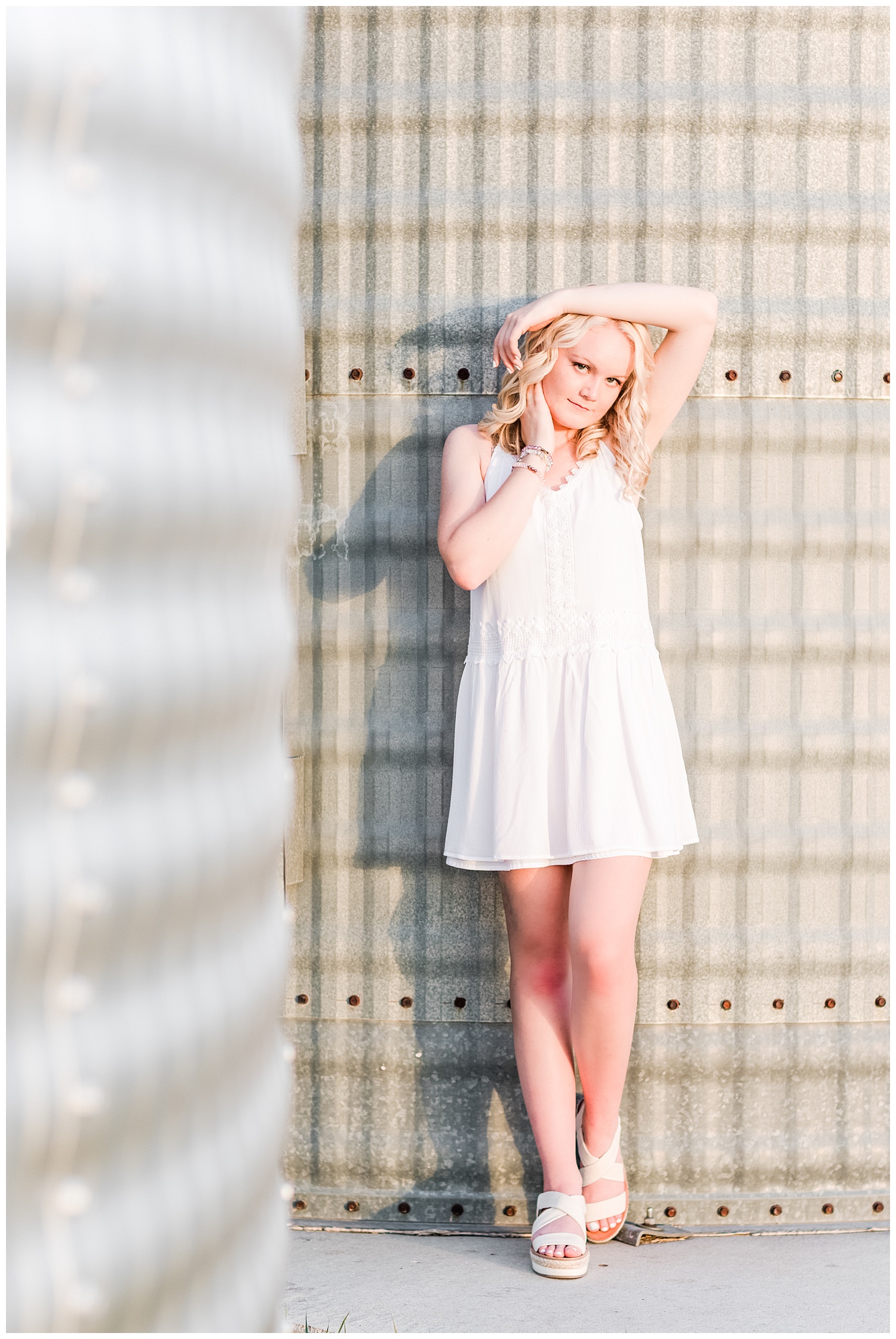 Senior girl Molly wearing a white dress leaning against a grain bin | CB Studio
