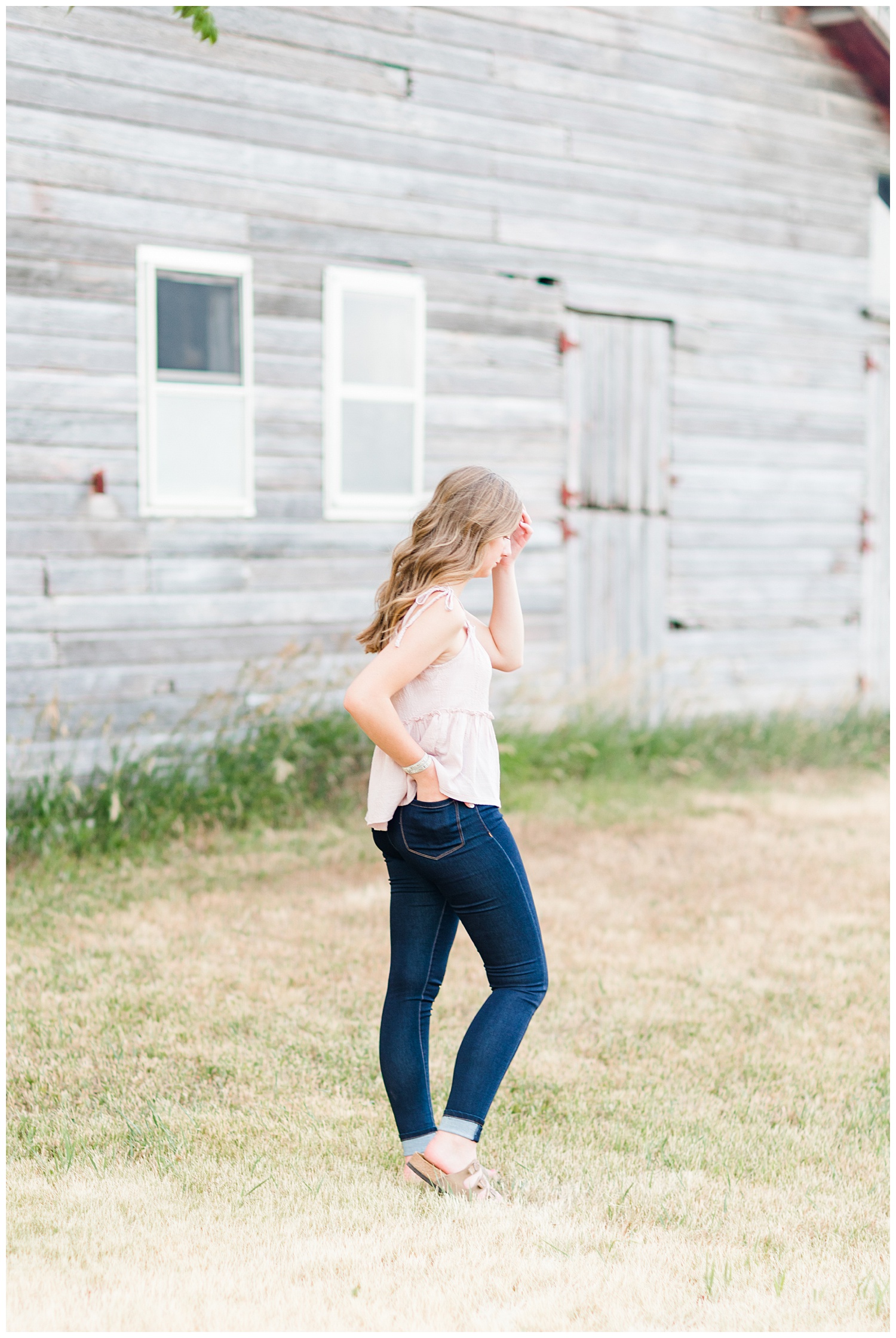 Senior Taylor brushes her hair aside as the wind blows with an old wooden barn in the background | CB Studio