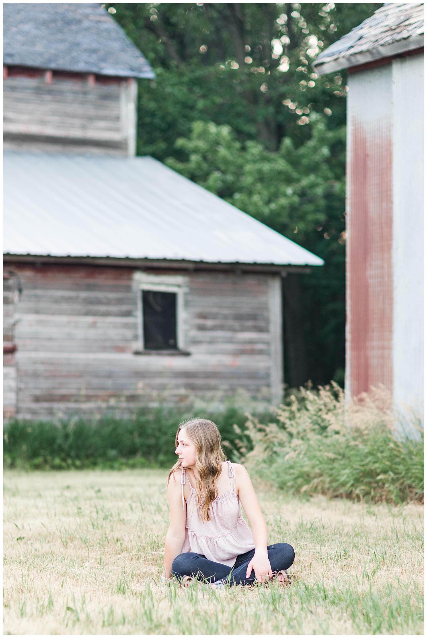 Senior Taylor sits in the grass with some old wood barns in the background | CB Studio