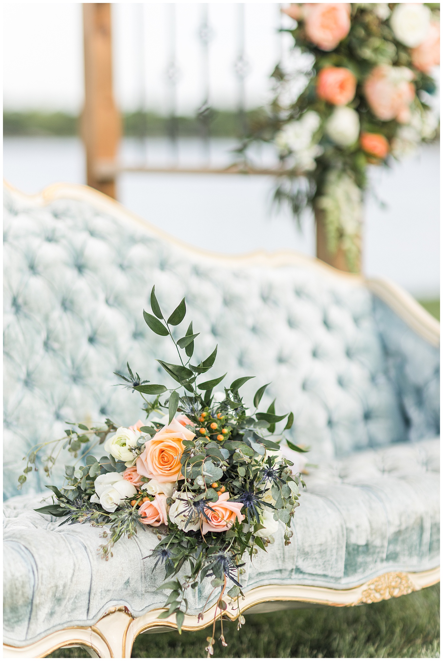 Peach and white rose wedding bouquet with white ranunculus and eucalyptus sitting on top of a dusty blue victorian couch | CB Studio