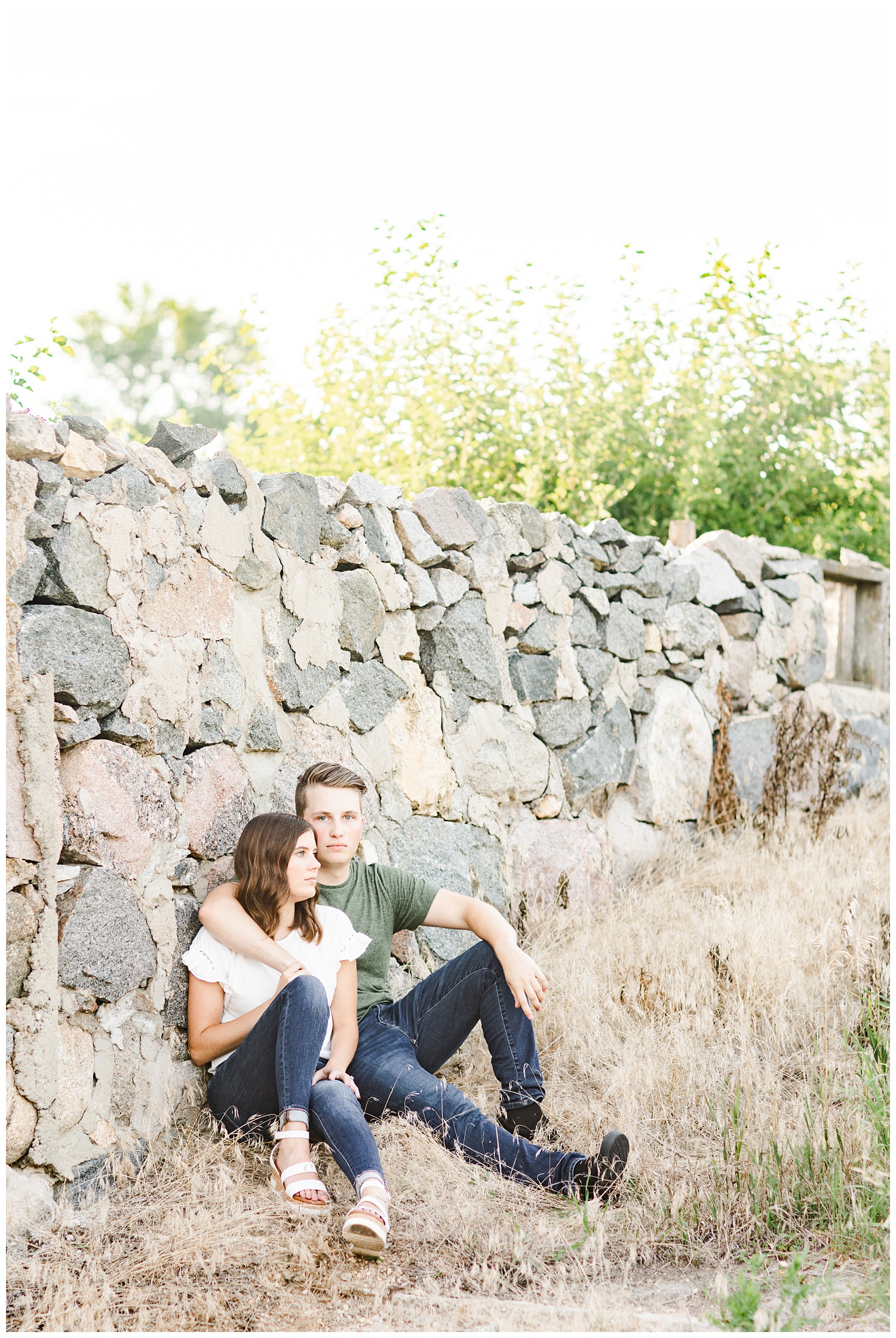 Luke wraps his arm around Jadi as they sit against an old stone wall | CB Studio