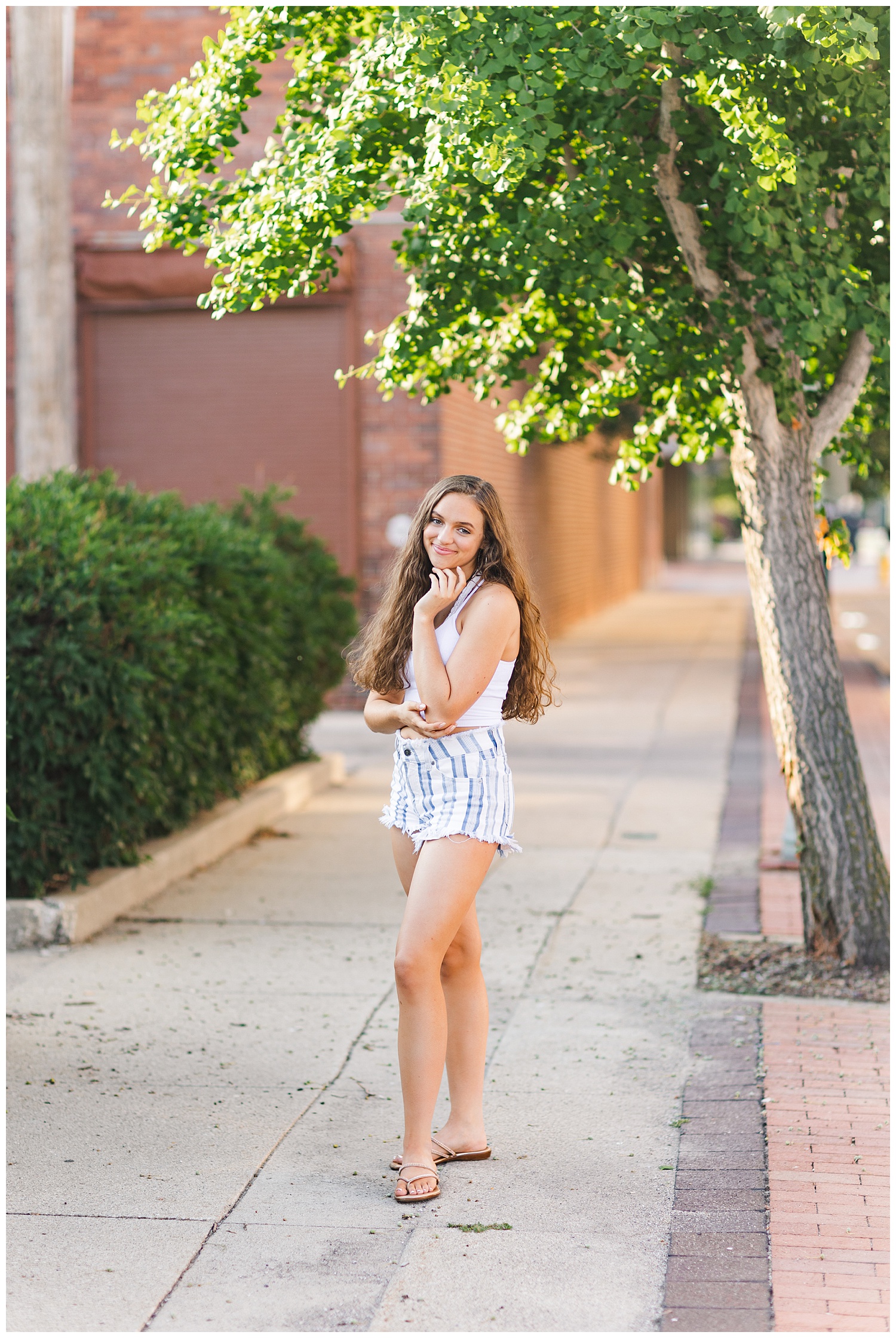 Senior Kennedy poses on a sidewalk lined with trees in downtown Fort Dodge | CB Studio