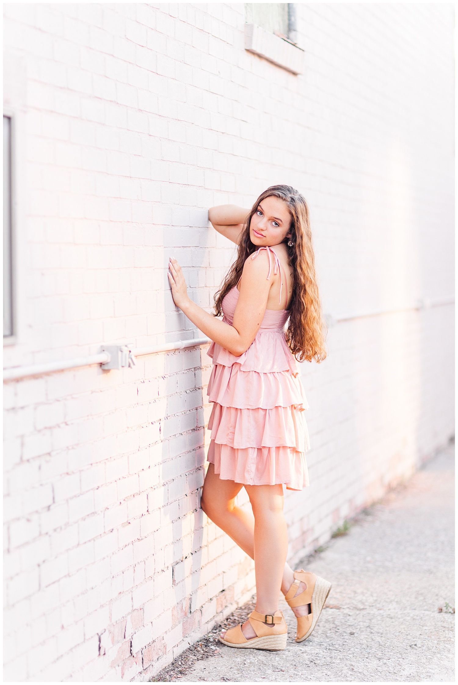 Senior Kennedy leans against a pink block wall in downtown Fort Dodge | CB Studio
