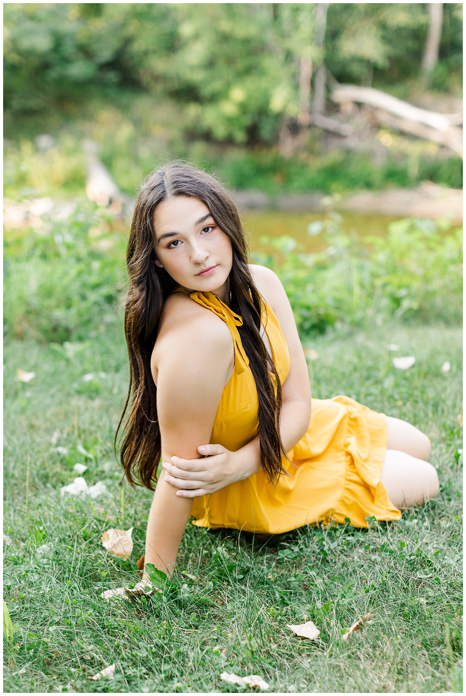 Laney, wearing a yellow dress, sits in the grass watching the river near Emmetsburg, IA | CB Studio