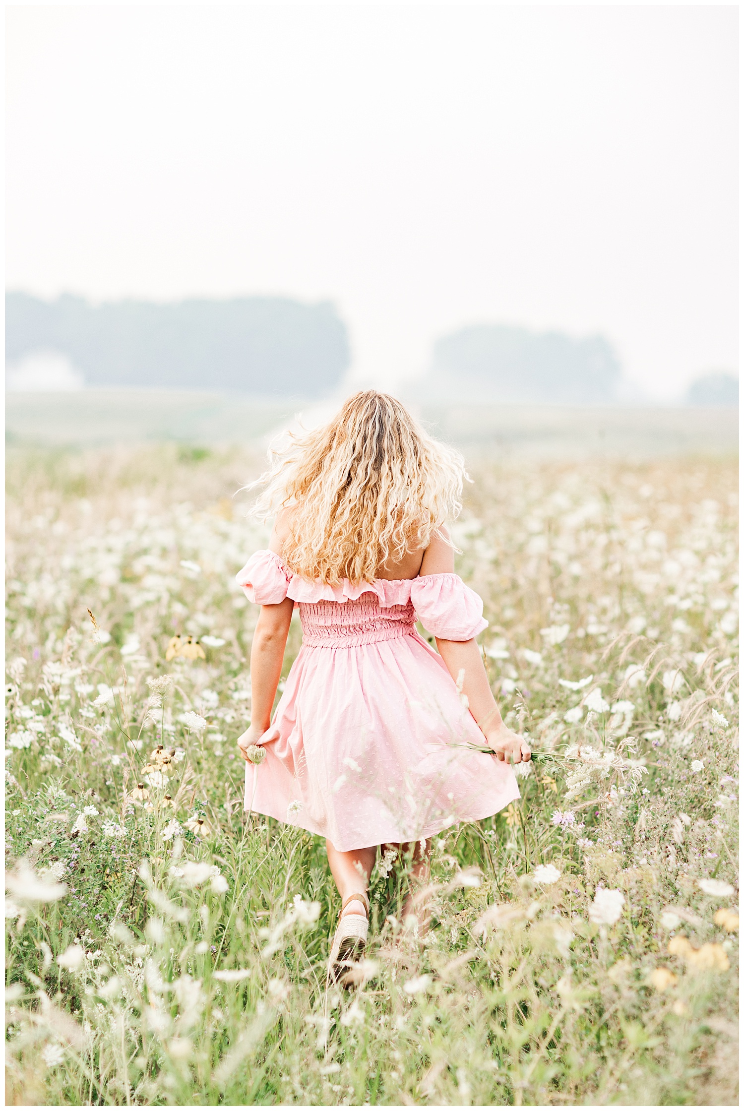 Senior Rachel wearing a light pink off the shoulder dress runs away in a wildflower field | CB Studio