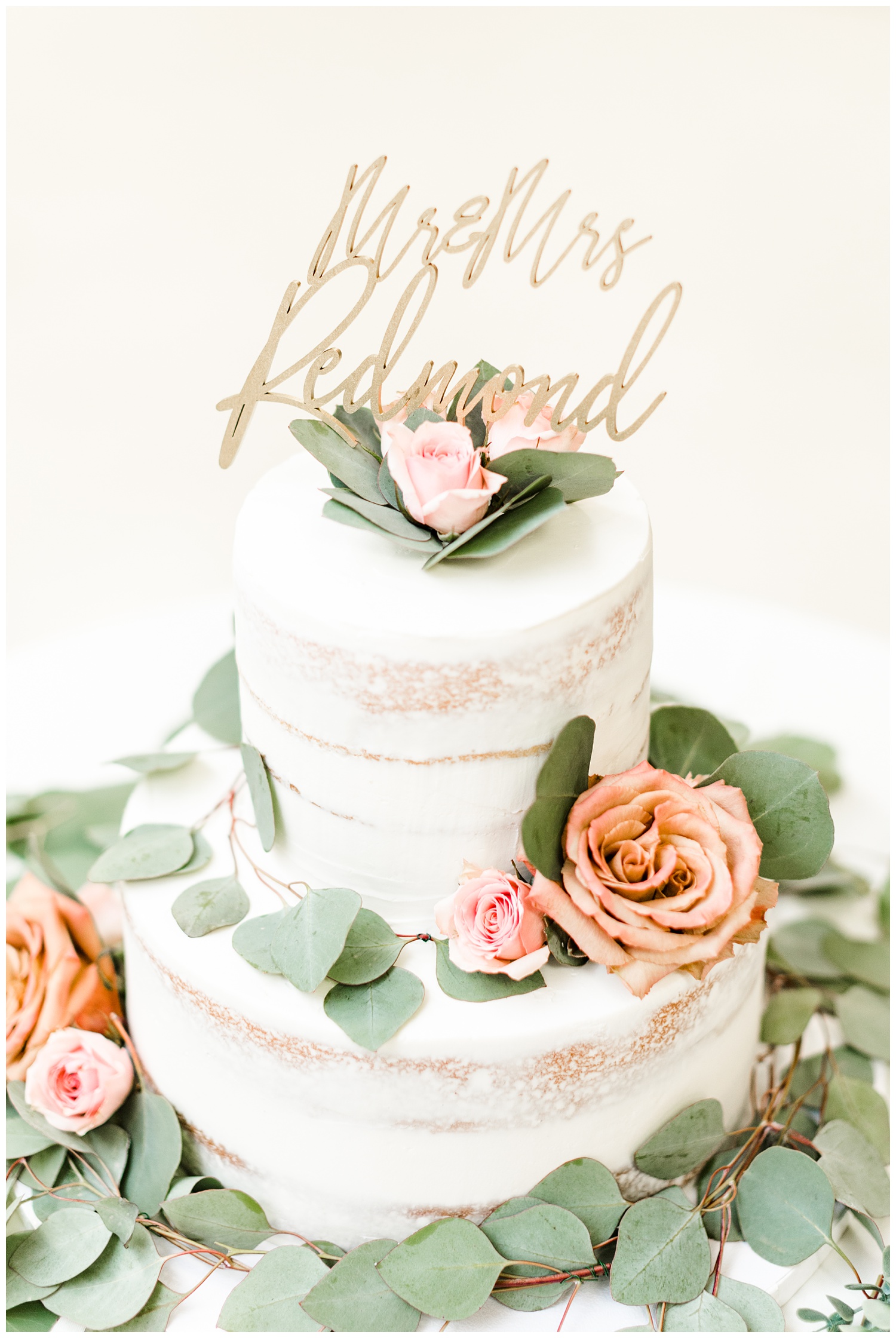 Naked wedding cake adorned with light pink and dusty orange roses as well as eucalyptus and a custom Mr. & Mrs. Redmond cake topper | CB Studio