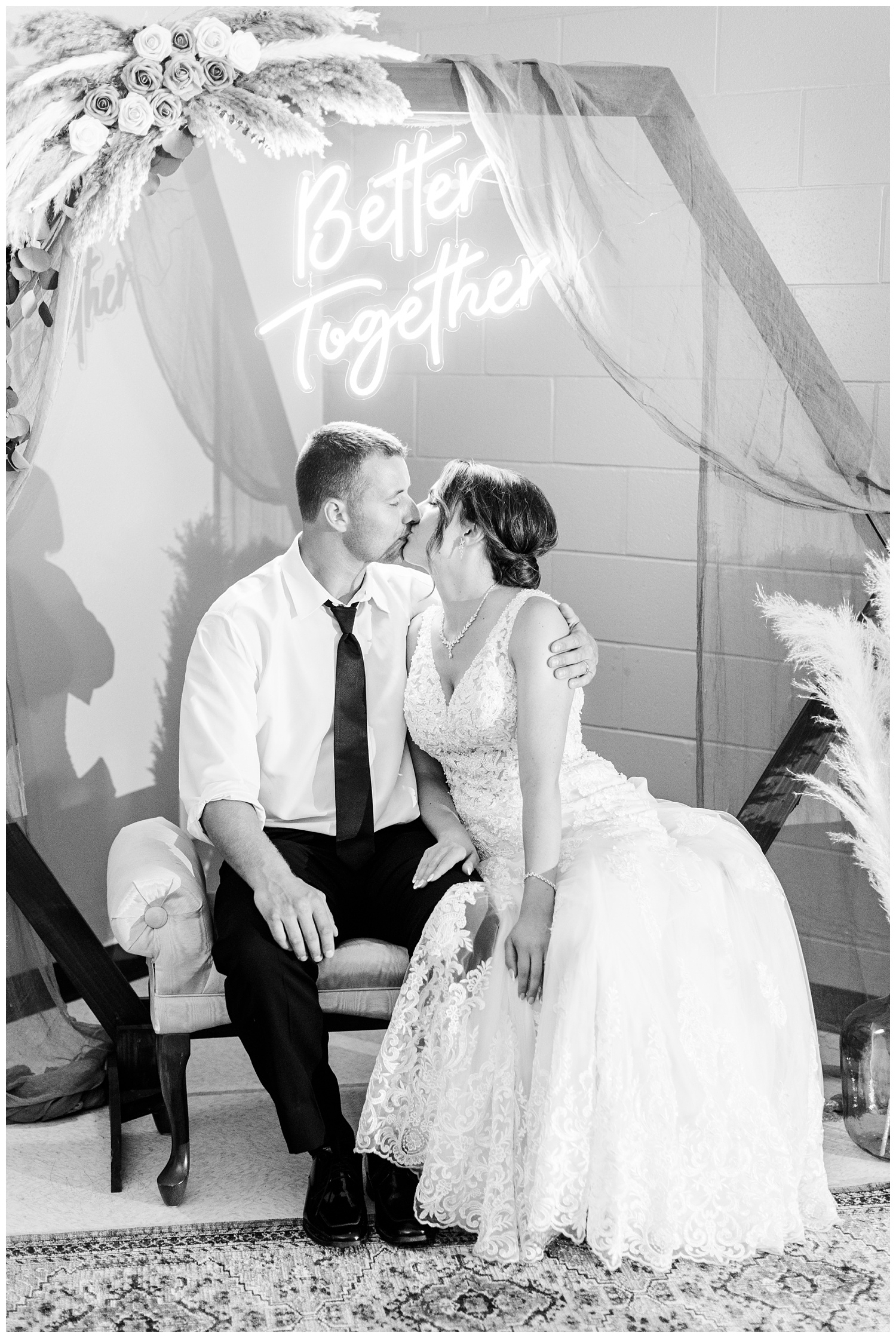 Mr. & Mrs. Redmond kiss under a custom boho themed photo backdrop featuring a wooden hexagon arch with draping cloths, "Better Together" neon sign, rose and pampas grass arrangements, antique rug and vintage settee | CB Studio