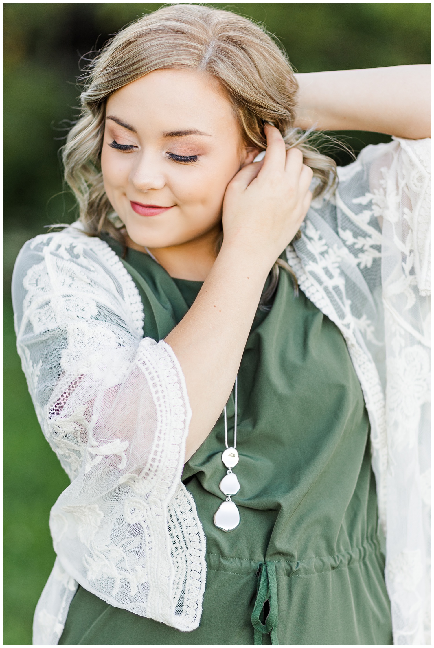 Cloey, wearing a green dress with a cream lace kimono, slowly tucks her hair behind her ear while looking down | CB Studio