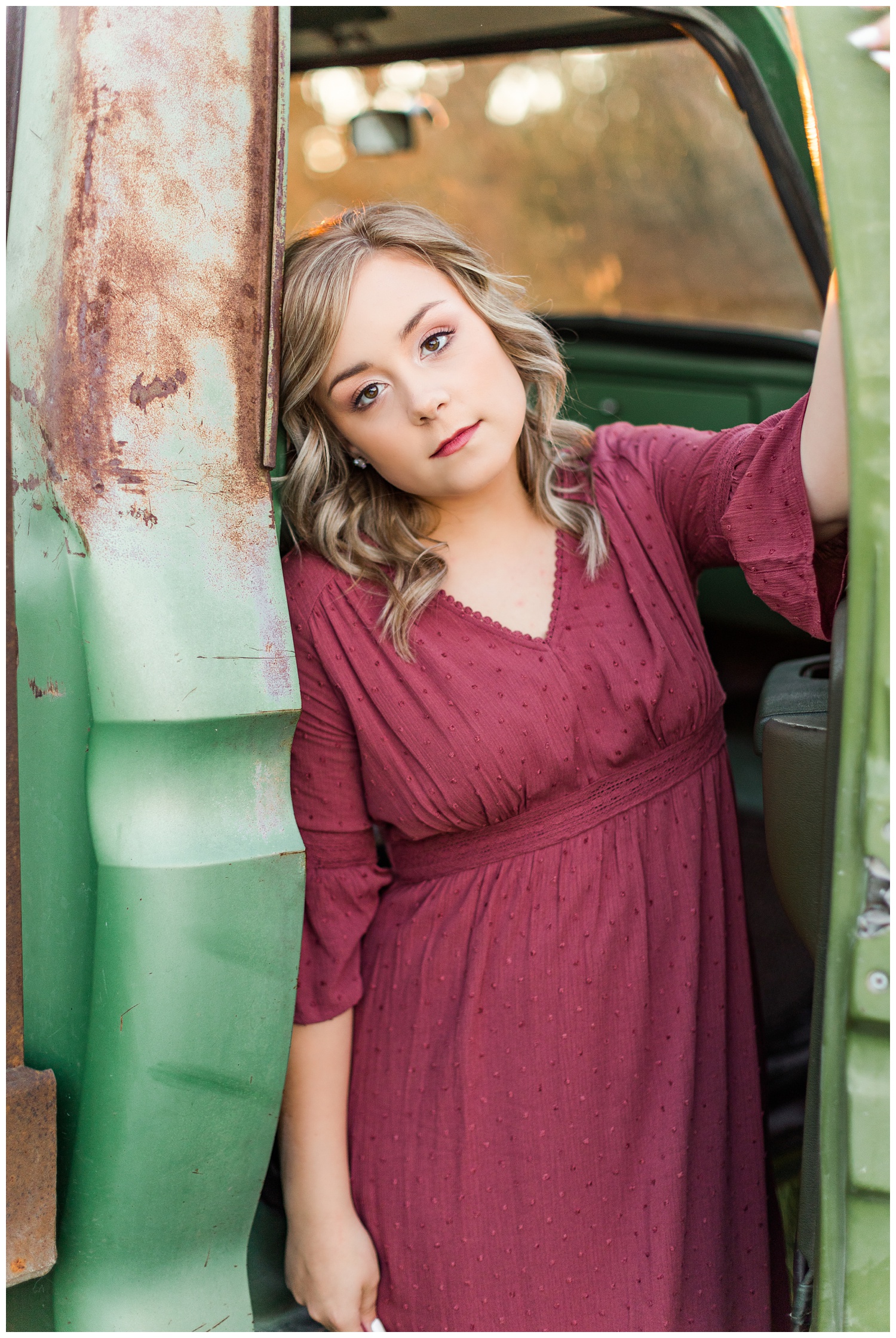 Cloey, wearing a vintage red dress, leans against the passenger doorway of an old rusty truck | CB Studio