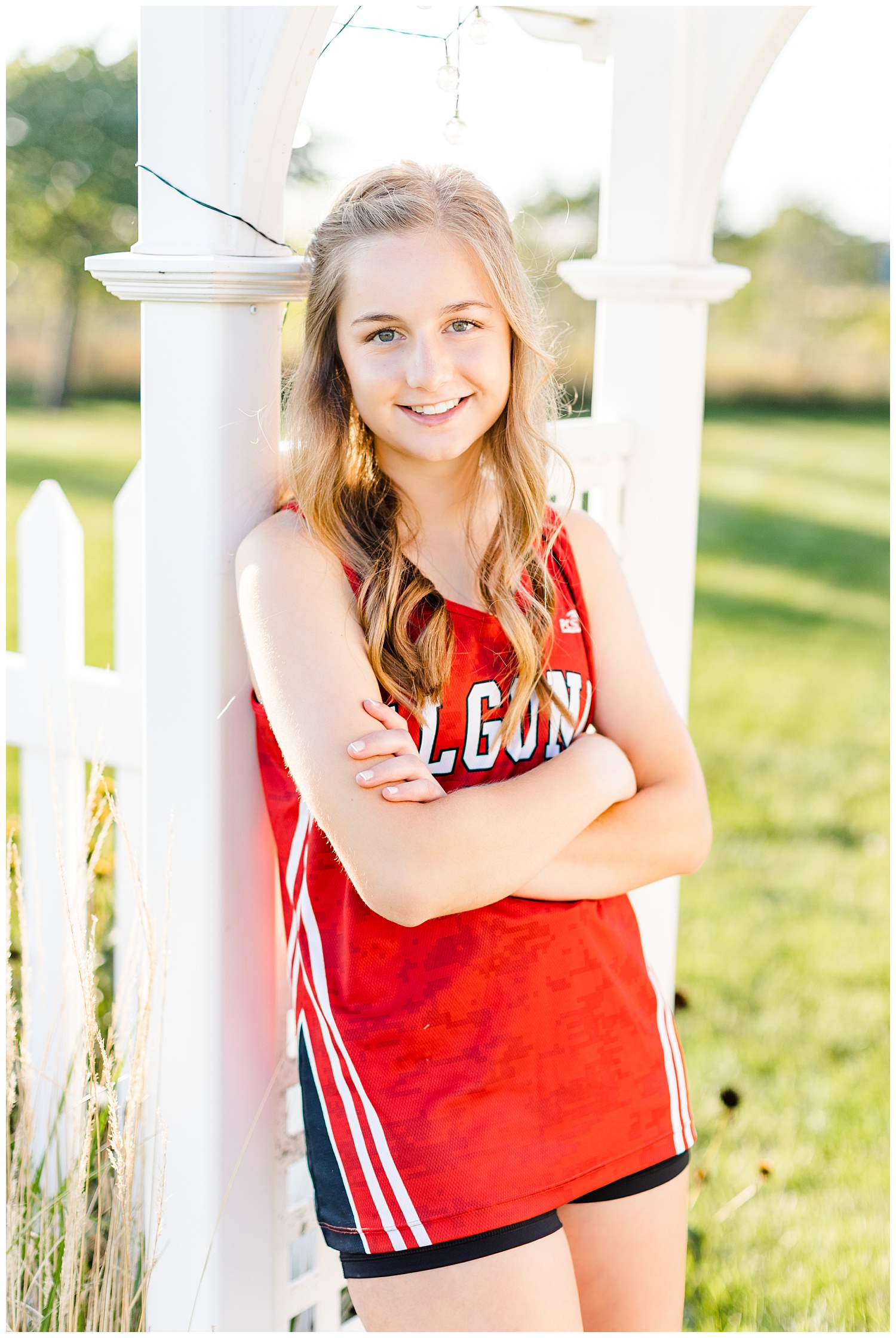 Taylor leans against a white arbor in her front yard wearing an Algona High cross country jersey | CB Studio