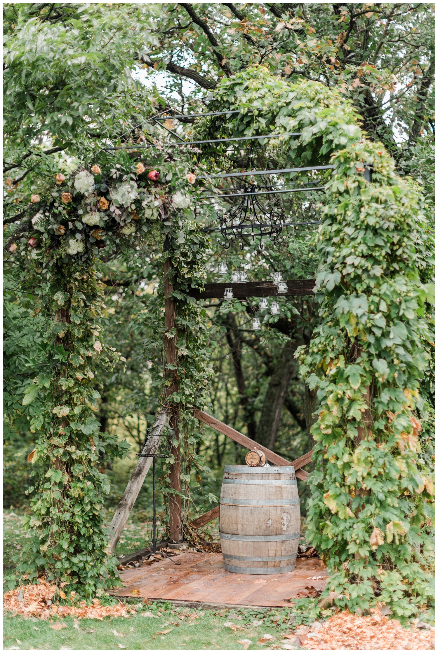 Wedding ceremony arch covered in florals and vines surrounded by oak trees featuring a whiskey barrel and candlelit chandelier at Diamond Oak Events | CB Studio