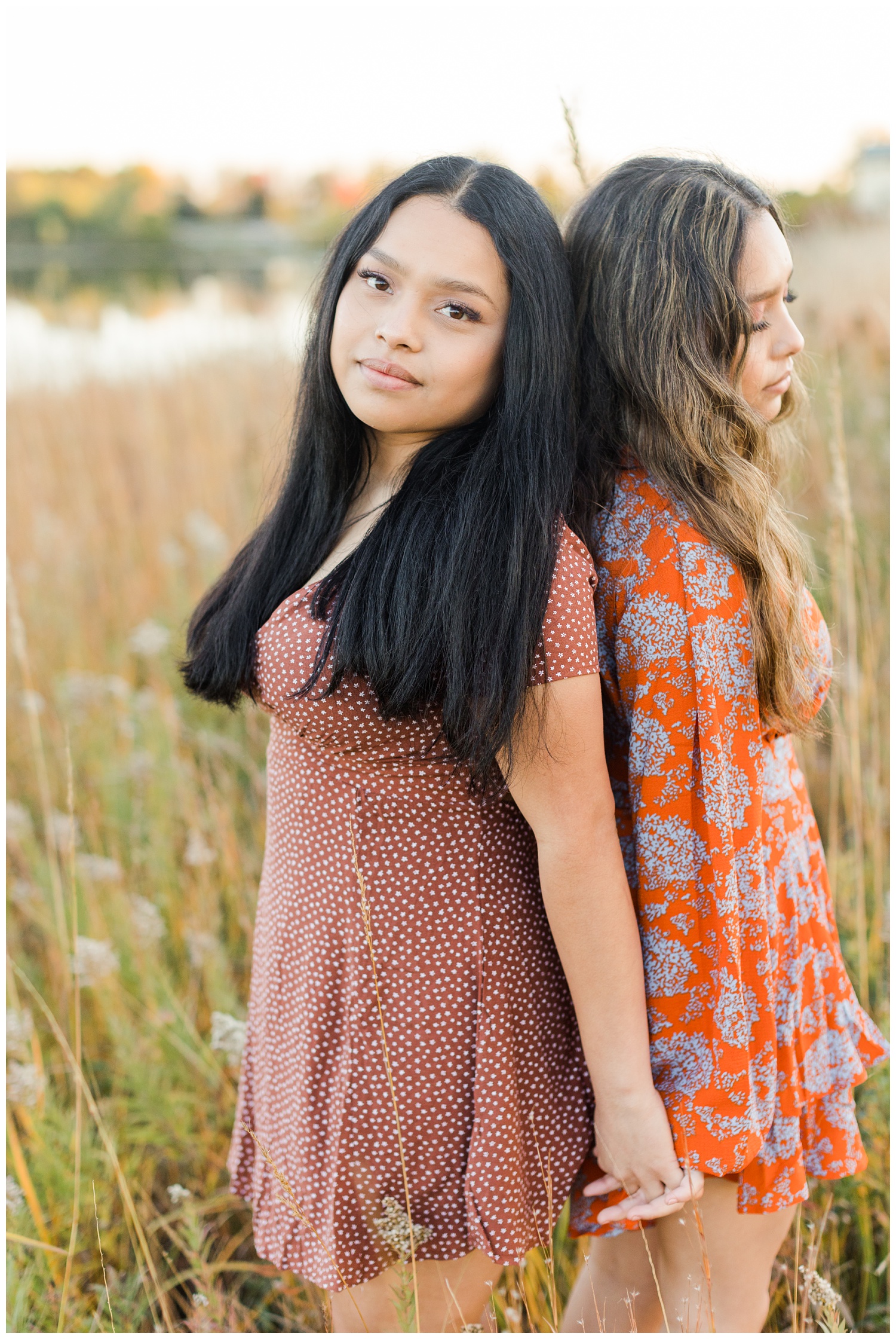 Twin sisters, Nicte and Sasil, lean against each other's back in a grassy pasture during fall in Iowa | CB Studio