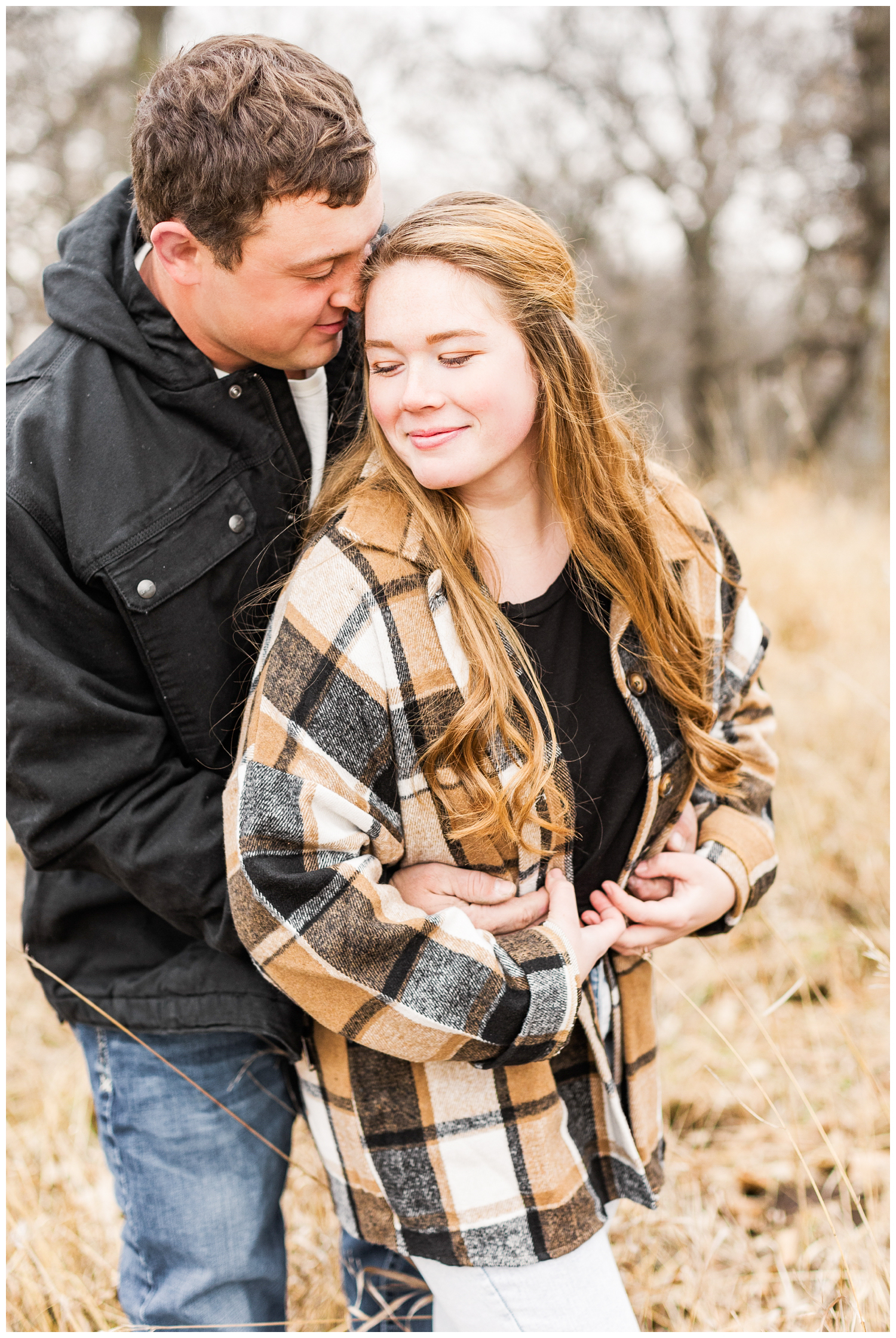Travis hugs his fiance Abi from behind in a grassy filed in Iowa in the middle of winter | CB Studio