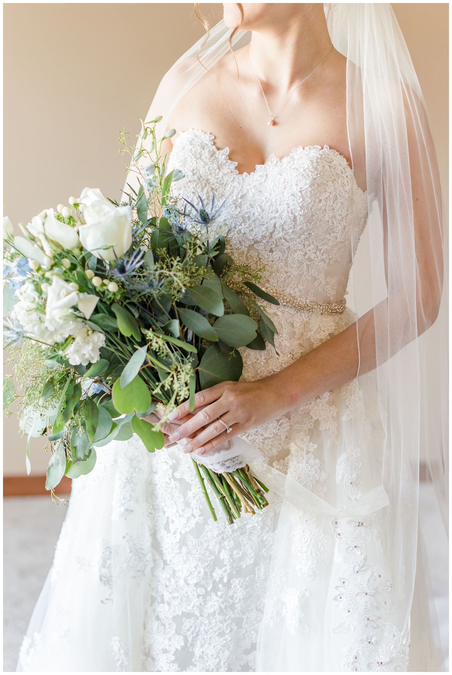 A bride wearing Sophia Tolli holds her loose gathered bouquet of white roses, sea holly and eucalyptus | CB Studio
