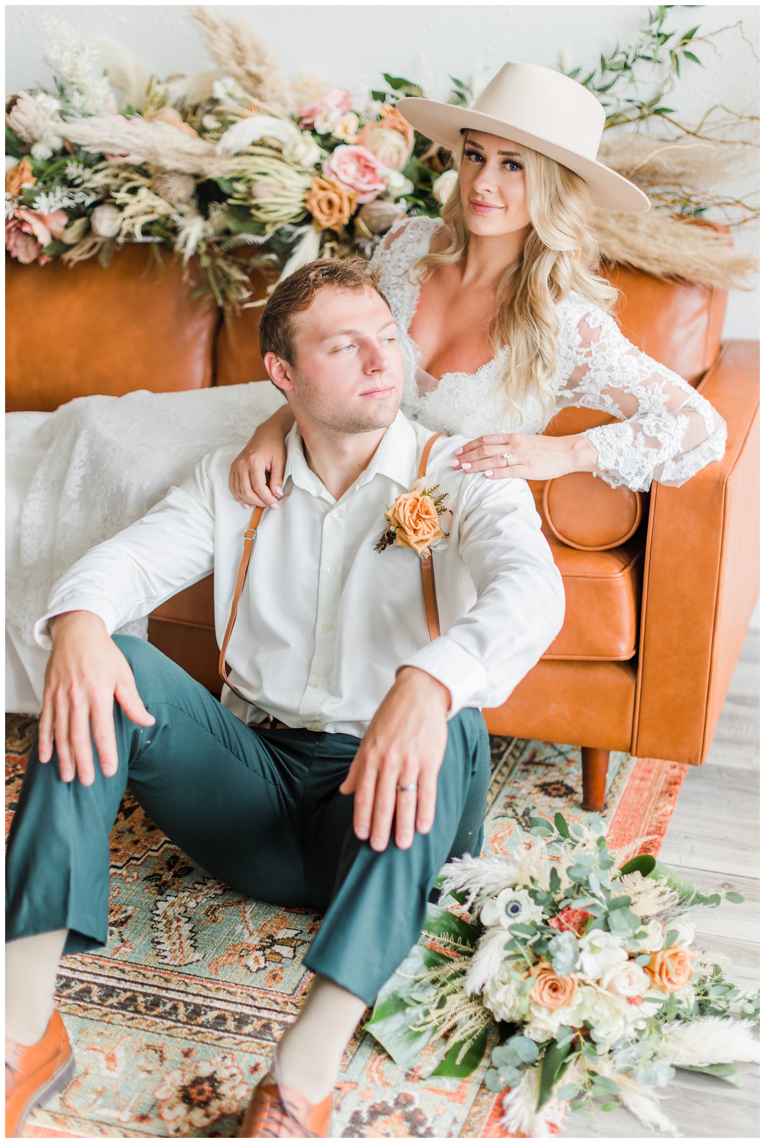 Boho bride and grown lounge on a leather couch surrounded by beautiful boho florals | CB Studio