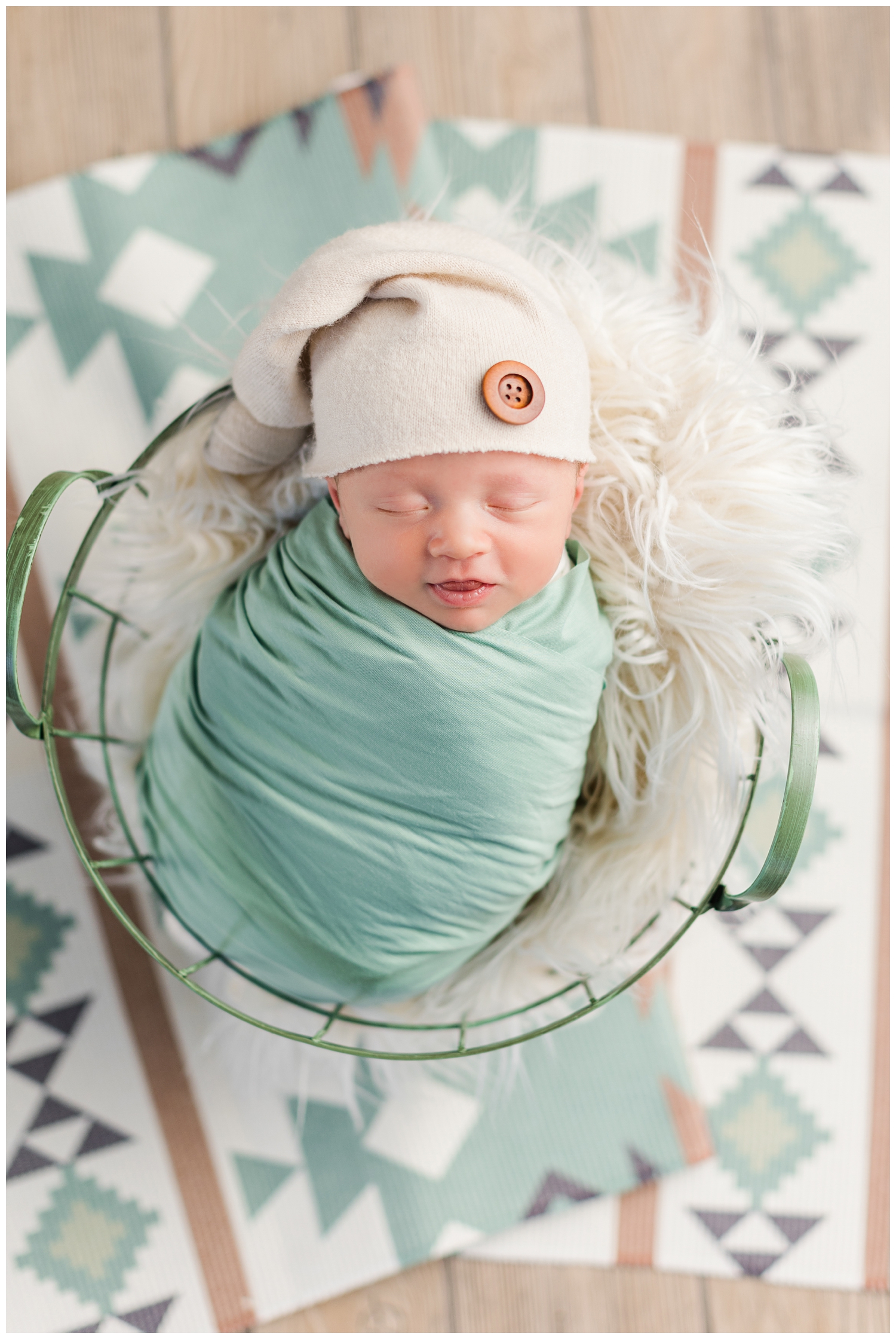 Baby Hudsyn wrapped in green and nestled in a green basket on top of a boho styled rug | CB Studio