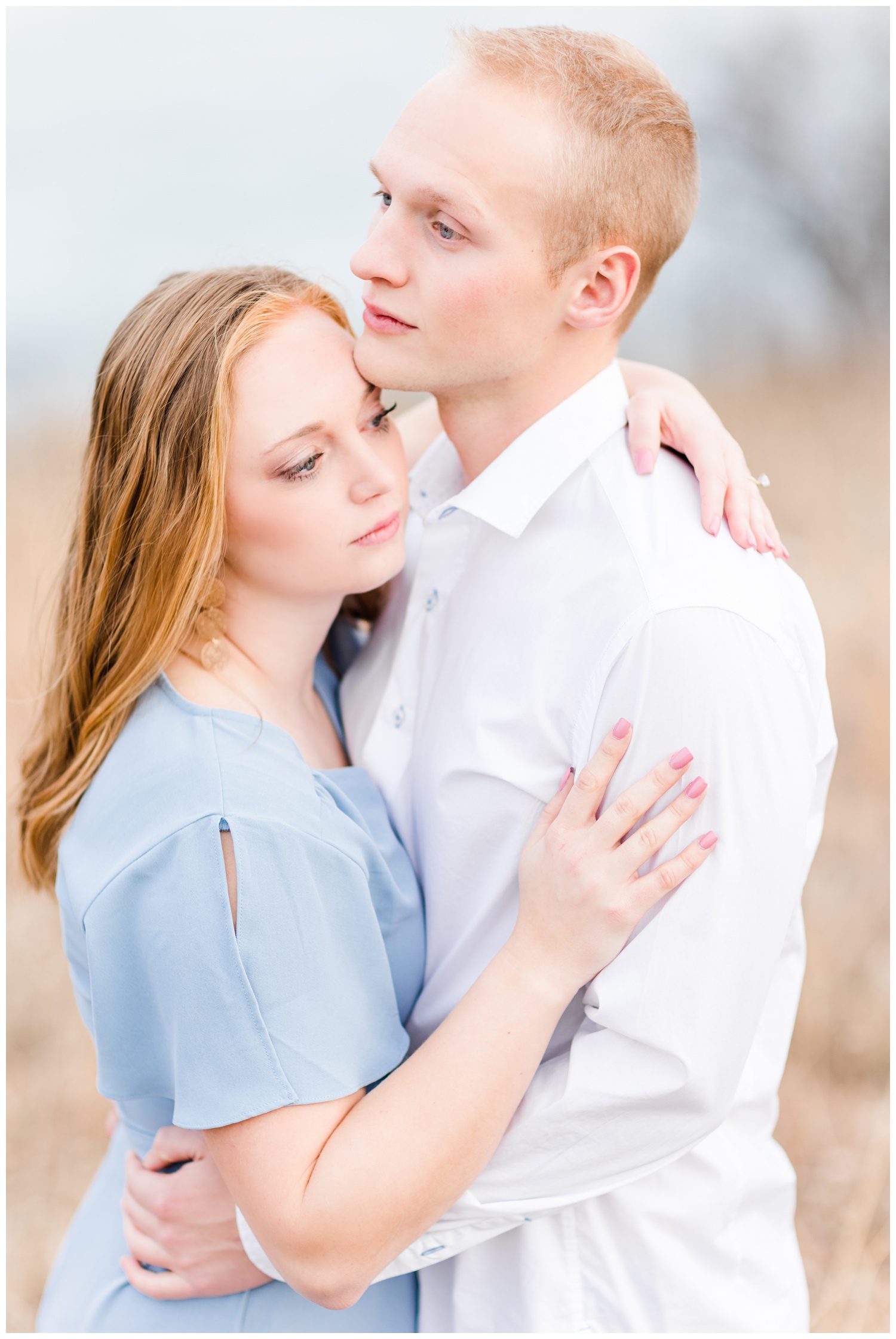 Brenna and Jacob embrace in the middle of a grassy field in front of a lake | CB Studio