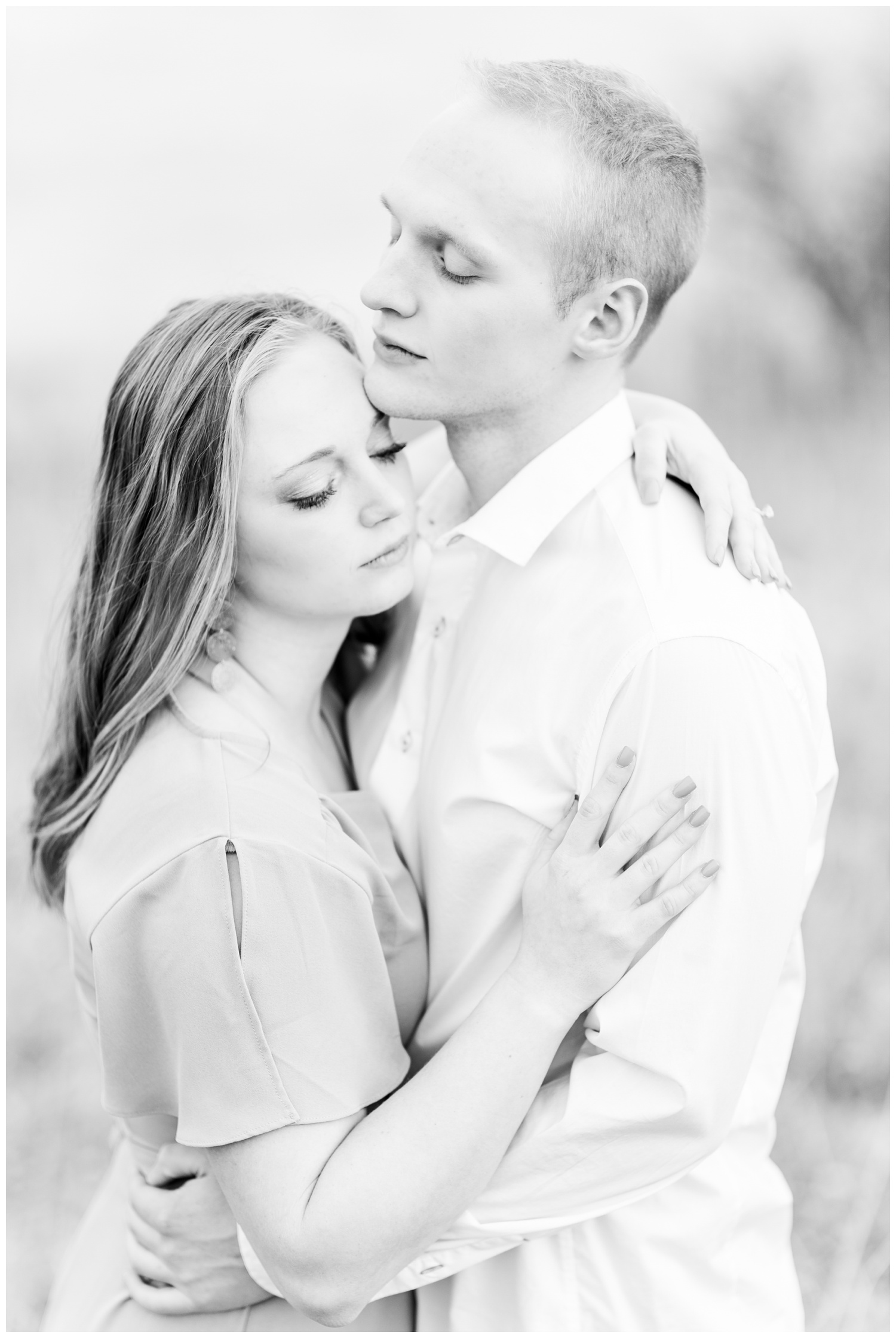 Brenna and Jacob embrace in the middle of a grassy field in front of a lake | CB Studio