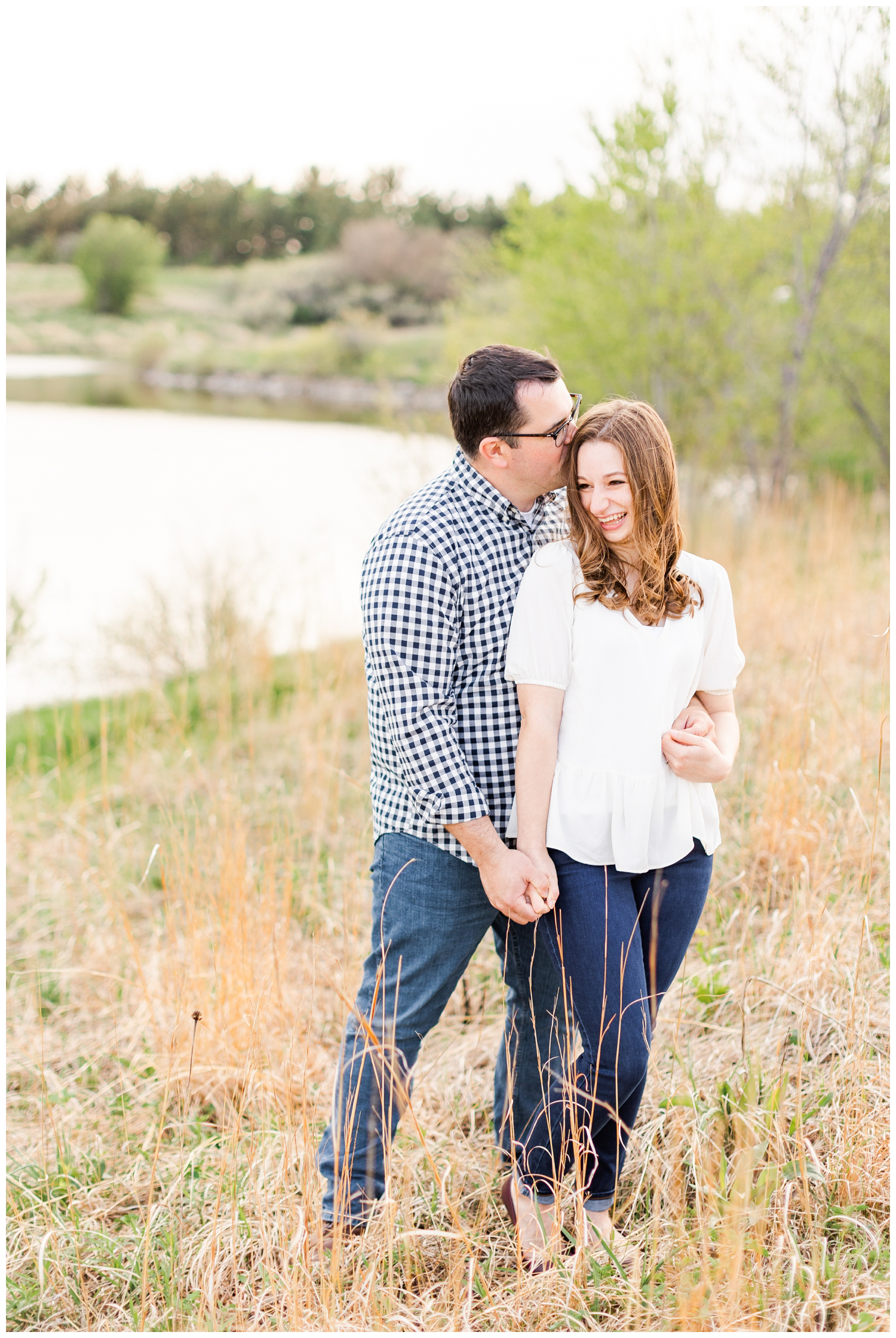 Joe and Leslie embrace in a grassy field with a lake in the background | CB Studio