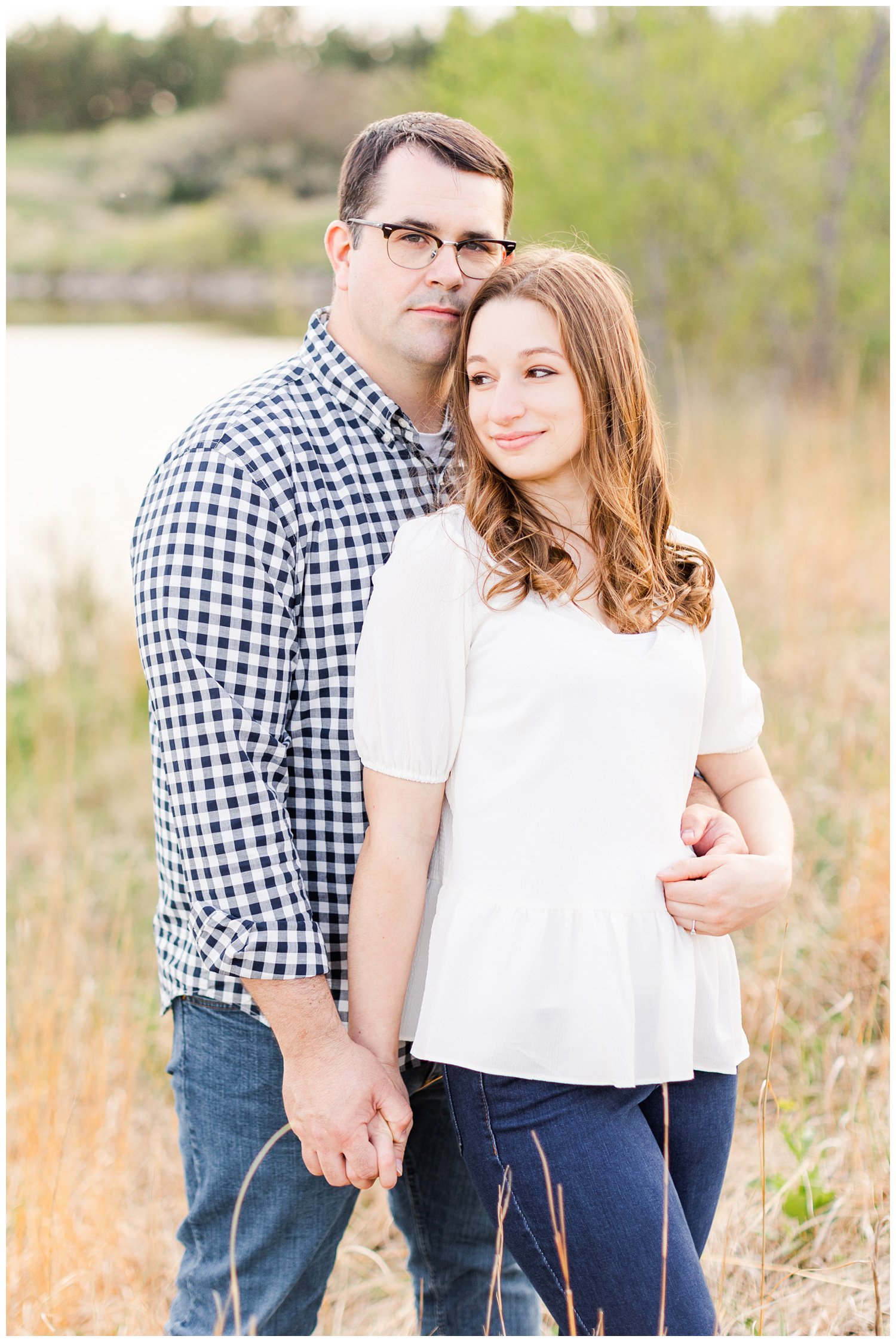 Joe and Leslie embrace in a grassy field with a lake in the background | CB Studio