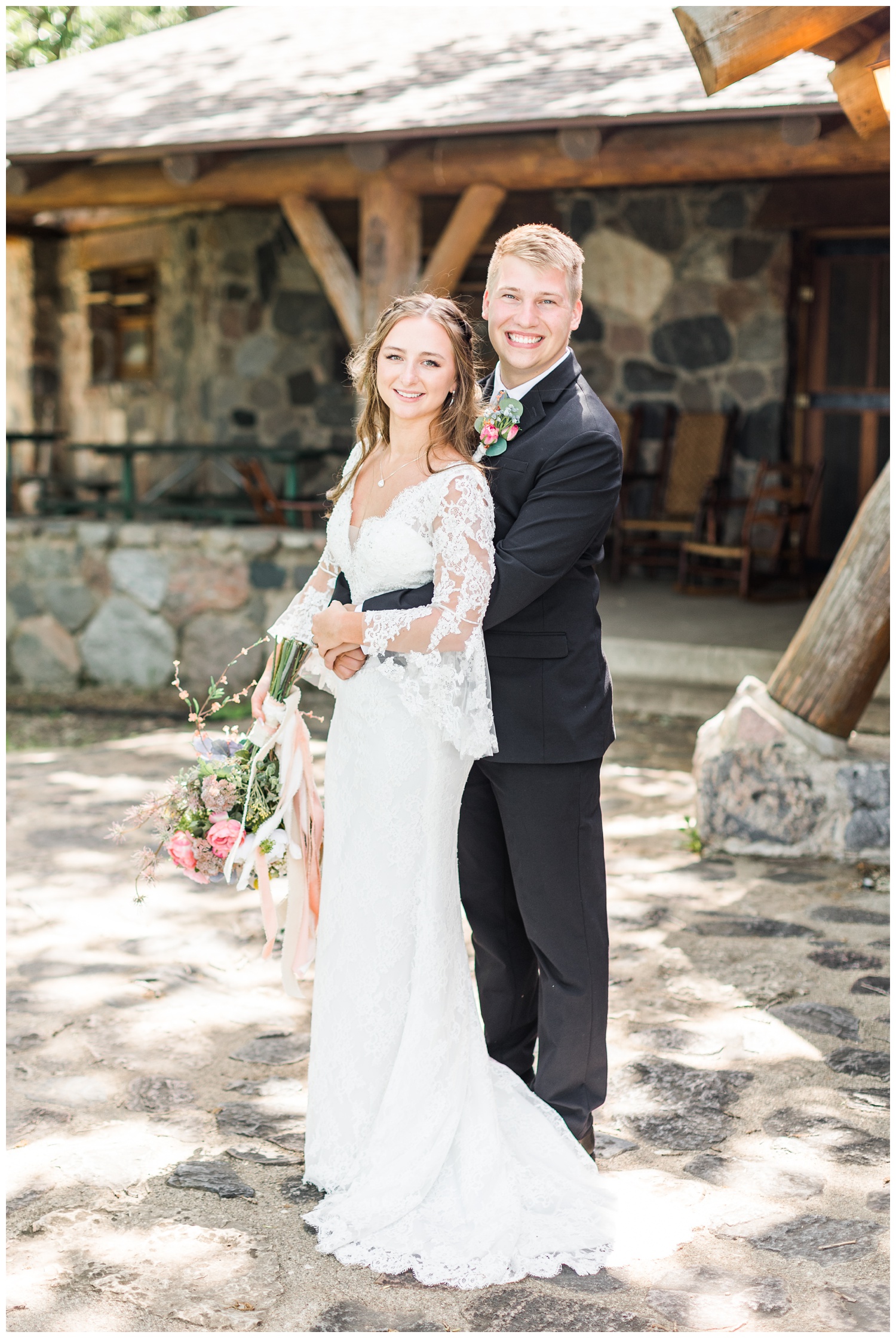 Ashlyn and Thad embrace in front of a rustic lodge on their wedding day | CB Studio