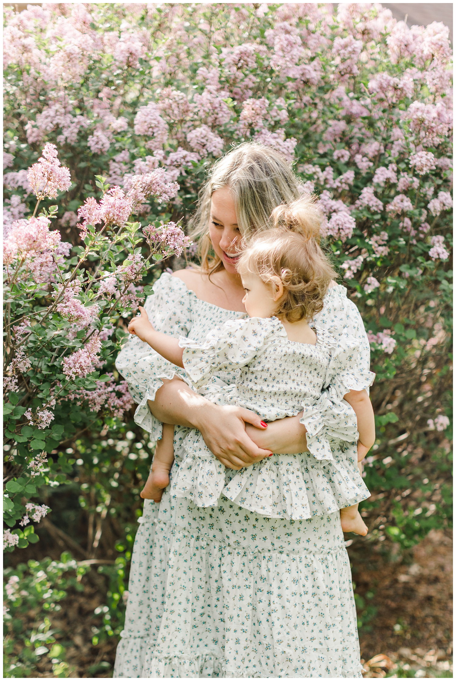 Abby snuggles her little girl near a lilac bush in the soft morning light, both wearing matching Ivy City Co dresses | CB Studio