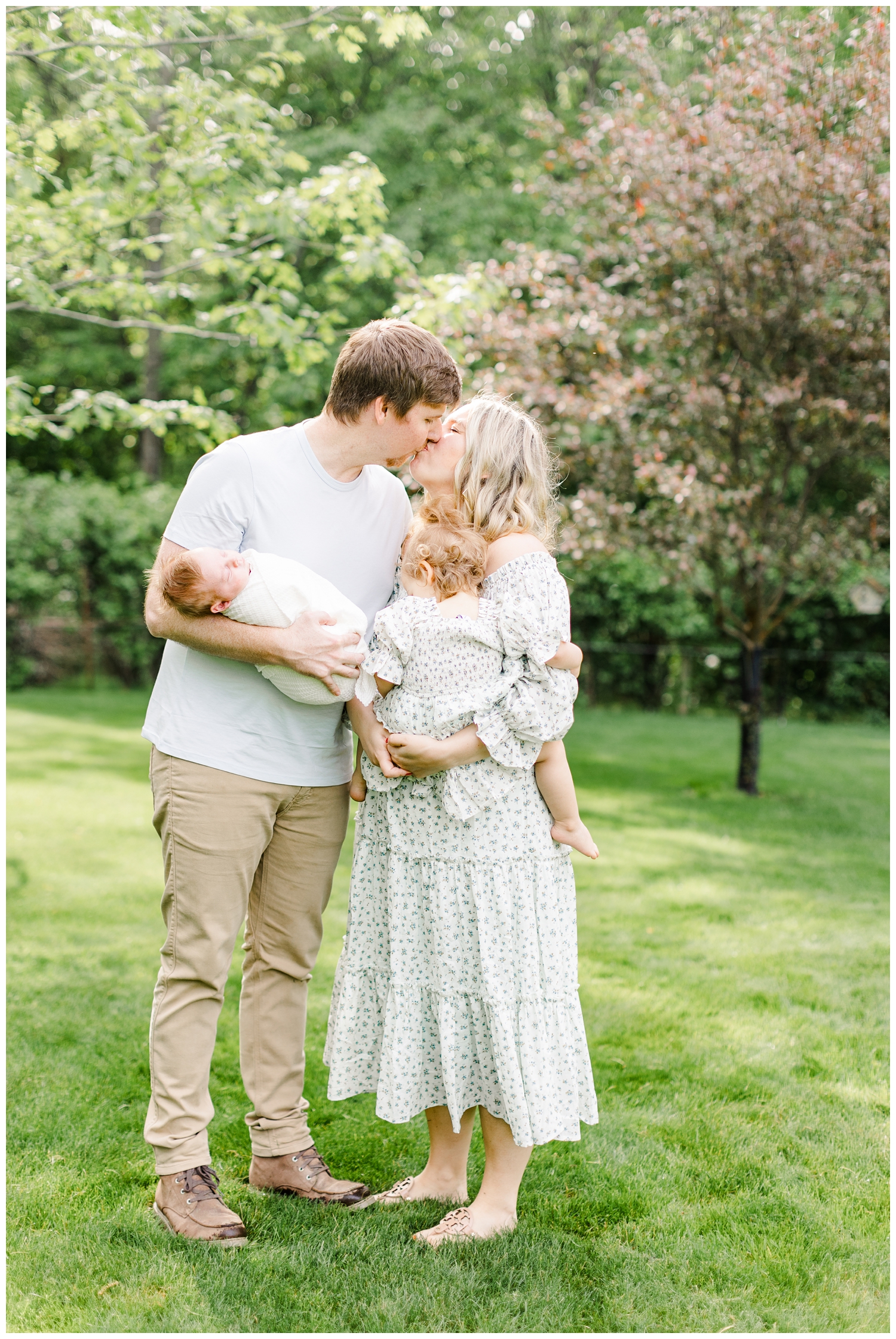 Abby and Derek share a kiss in the soft morning light while holding their small children | CB Studio
