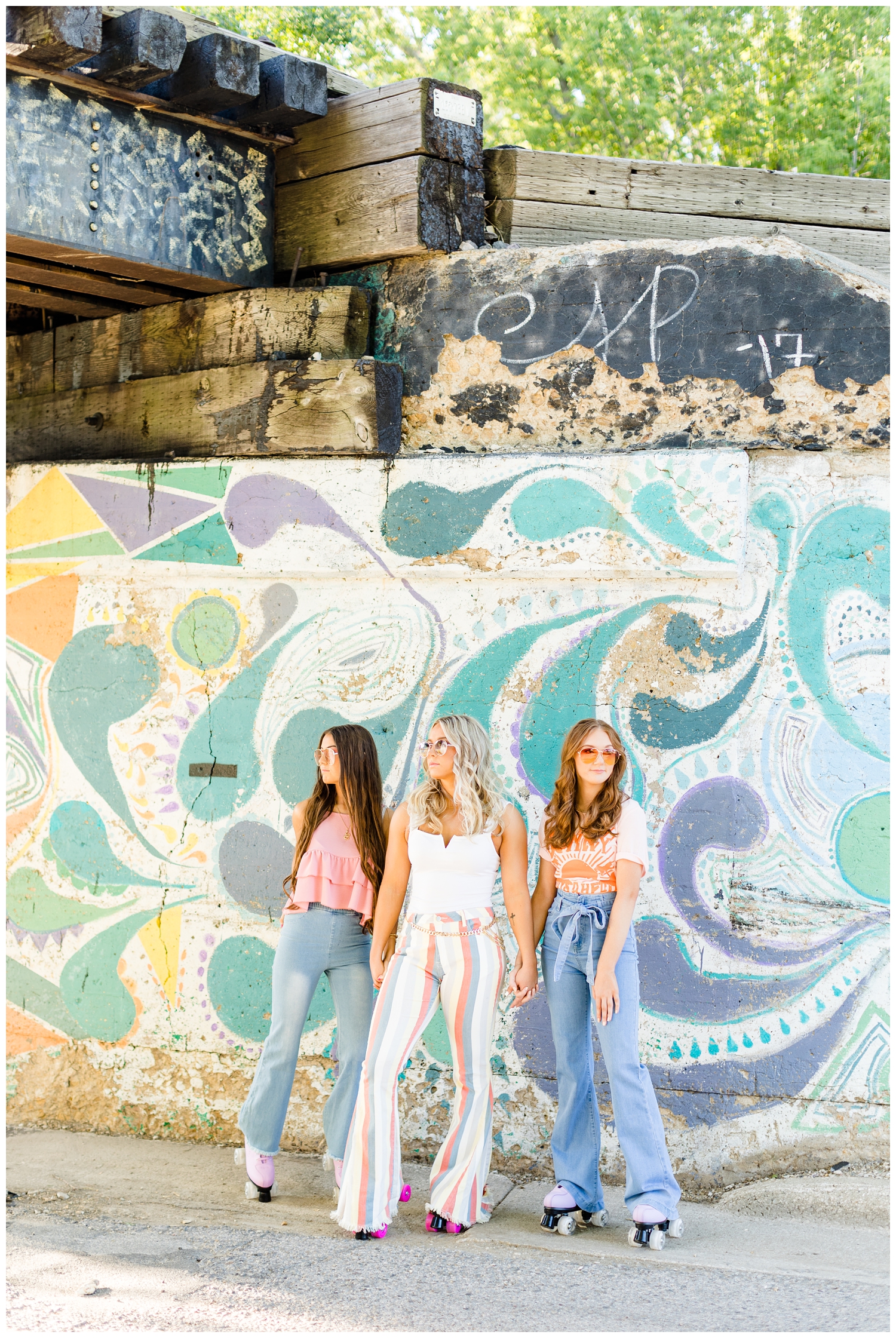 Olivia, Shelby and Savannah stand in front of a brightly colored graffiti wall dressed in modern 70s style and roller skates | CB Studio 