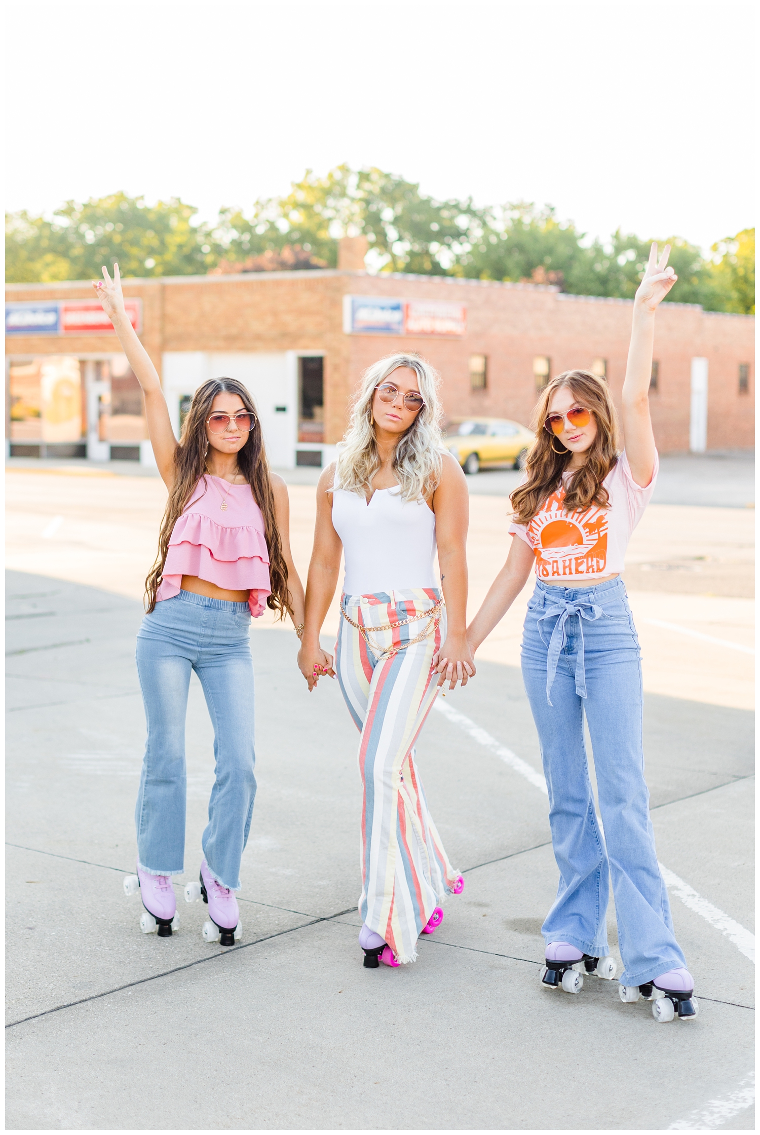 Olivia, Shelby and Savannah stand in a desolate parking lot holding peace signs dressed in modern 70s style and roller skates | CB Studio 