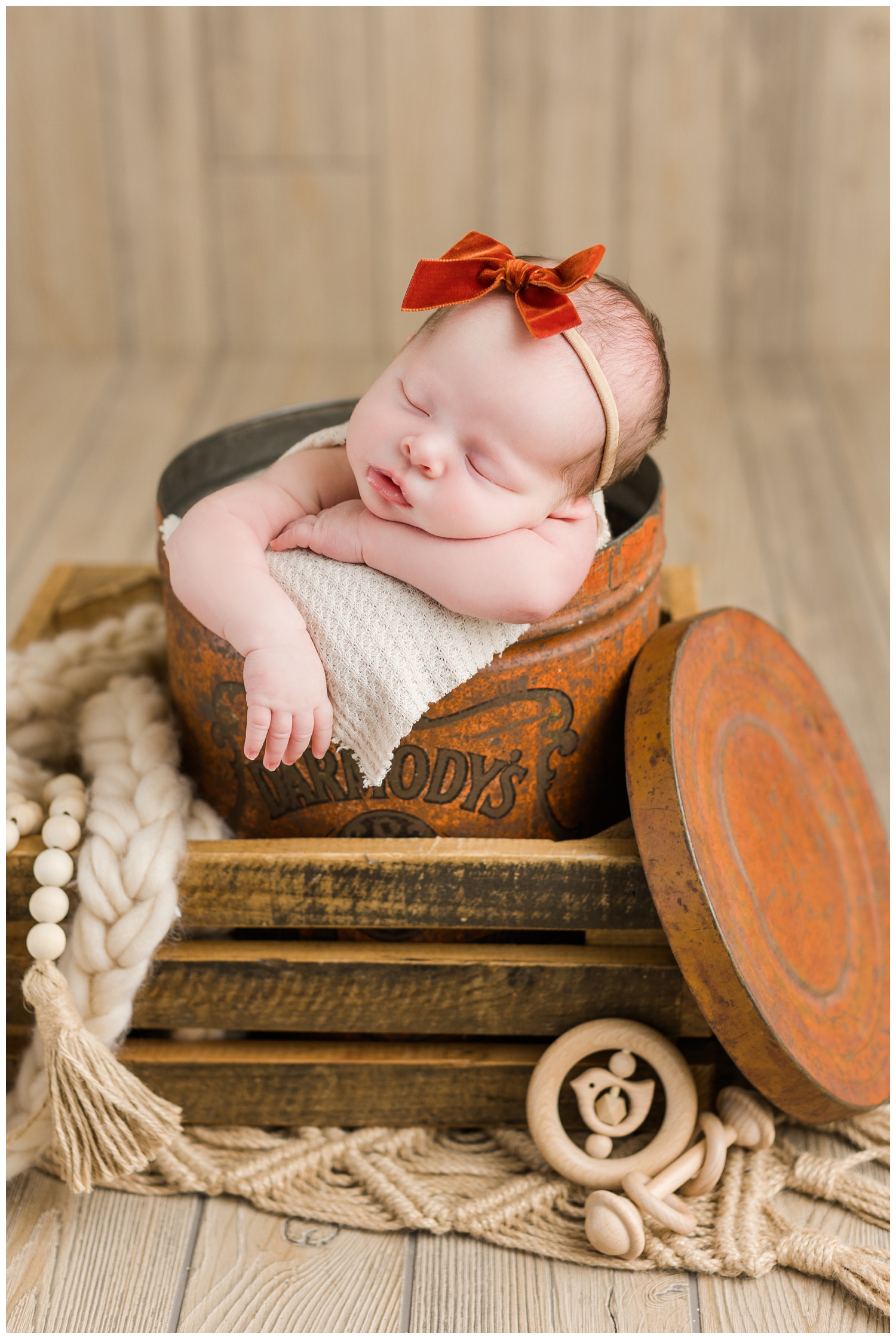 Baby Shae nestled in a rust color vintage tin surrounded by wooden rattles and a boho knit rug | CB Studio