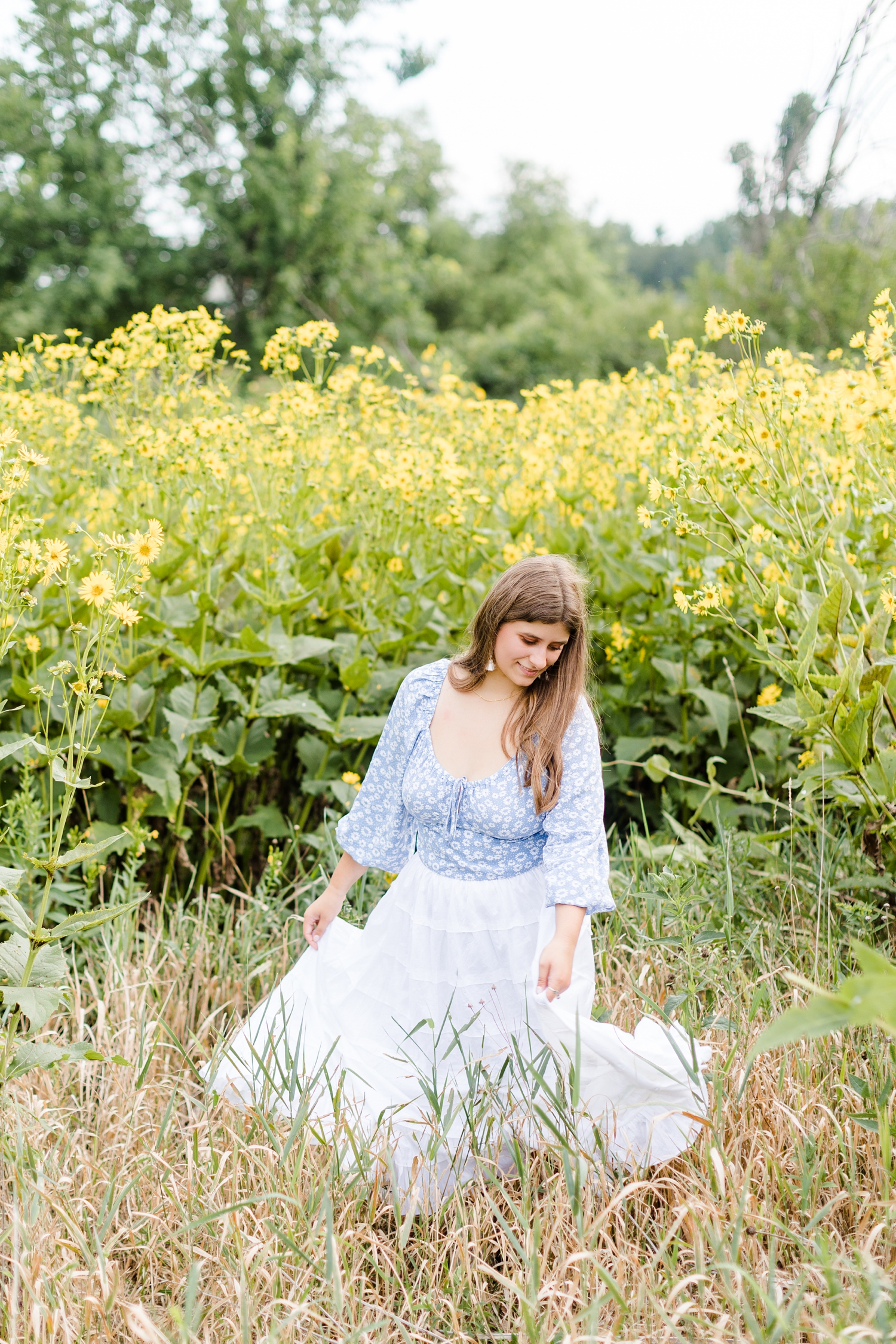 Caitlin twirls in a field of yellow wildflowers wearing a baby blue boho pheasant top and a white flowy skirt | CB Studio