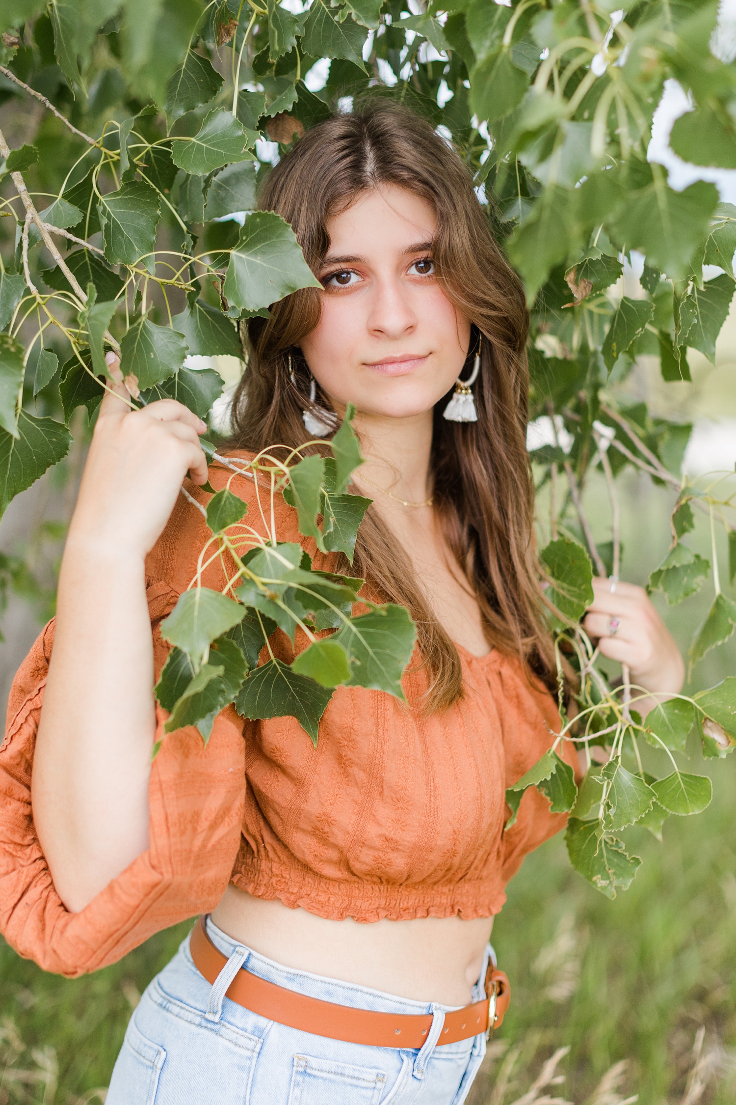 Caitlin stands by a low lying tree branch with leaves surrounding her wearing a boho pheasant top and jeans | CB Studio