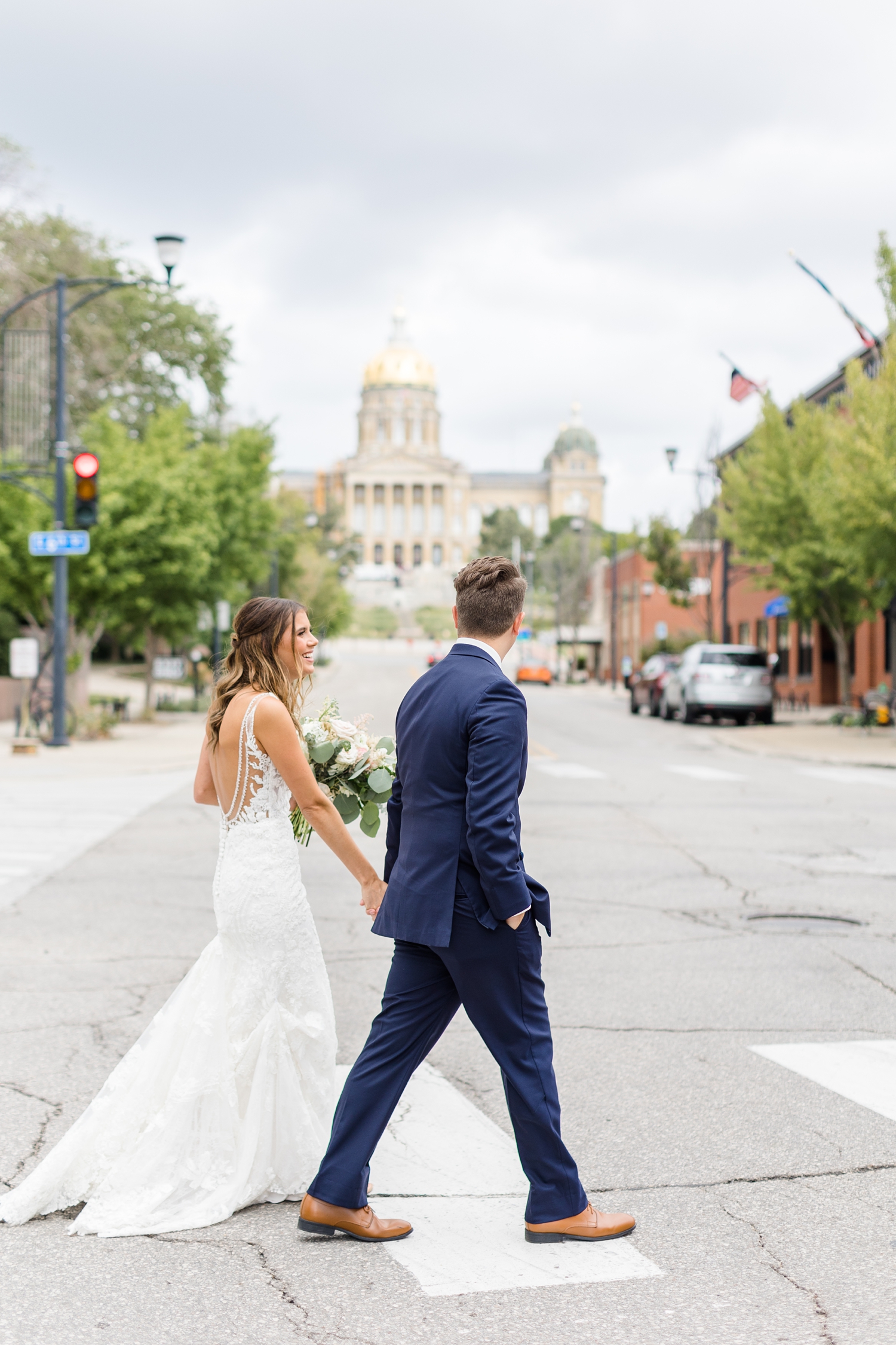 Bride and groom walk across the street in downtown Des Moines with the Iowa state capitol in the background | CB Studio